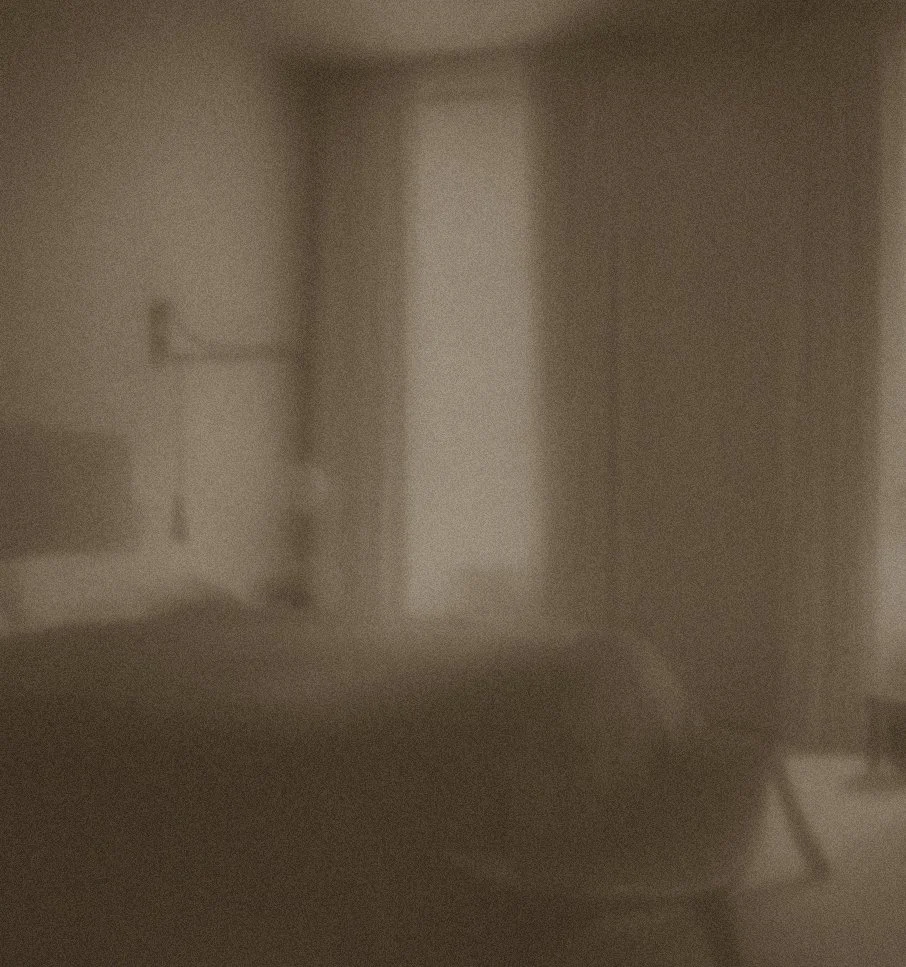 A blurry, dimly lit room with an indistinct object in the foreground and a doorway or open space in the background.