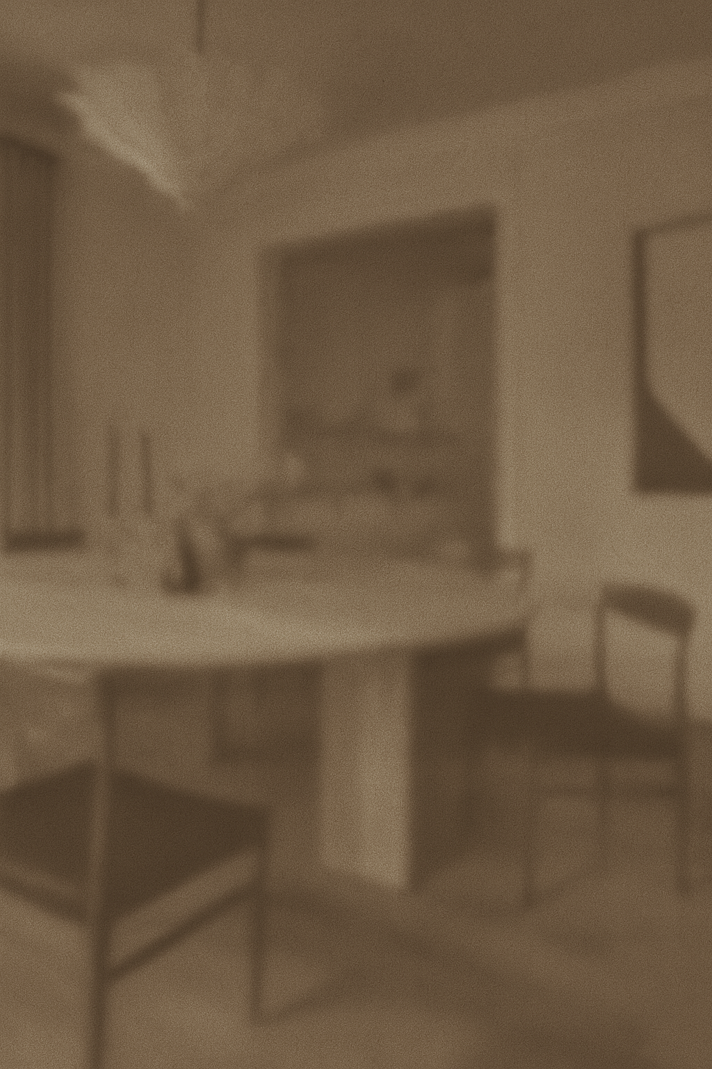 A blurred black-and-white interior of a room with a round table and chairs, and a framed portrait on the wall.