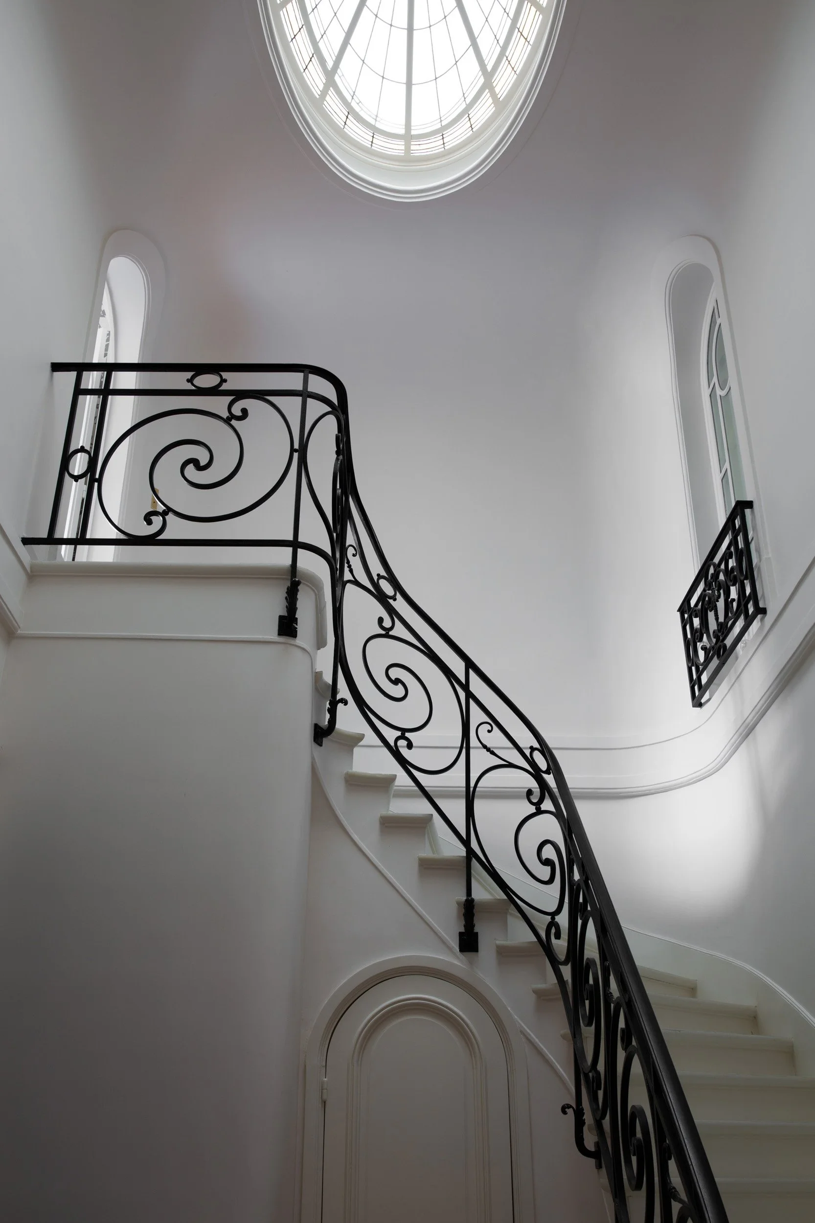 Interior view of a staircase with black wrought iron railing, white walls, and an overhead skylight with a glass dome.
