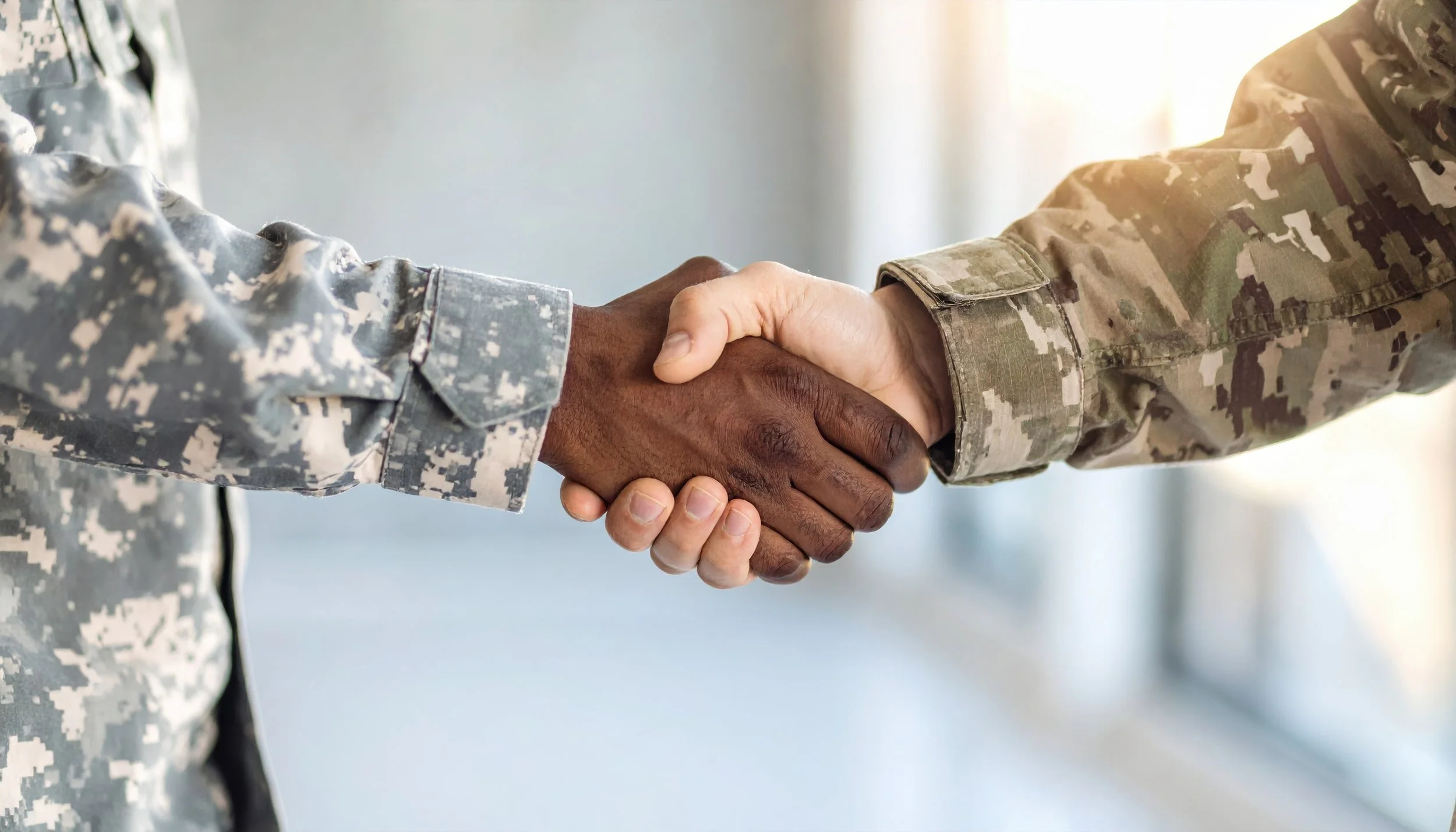 Two military personnel in camouflage uniforms shaking hands.