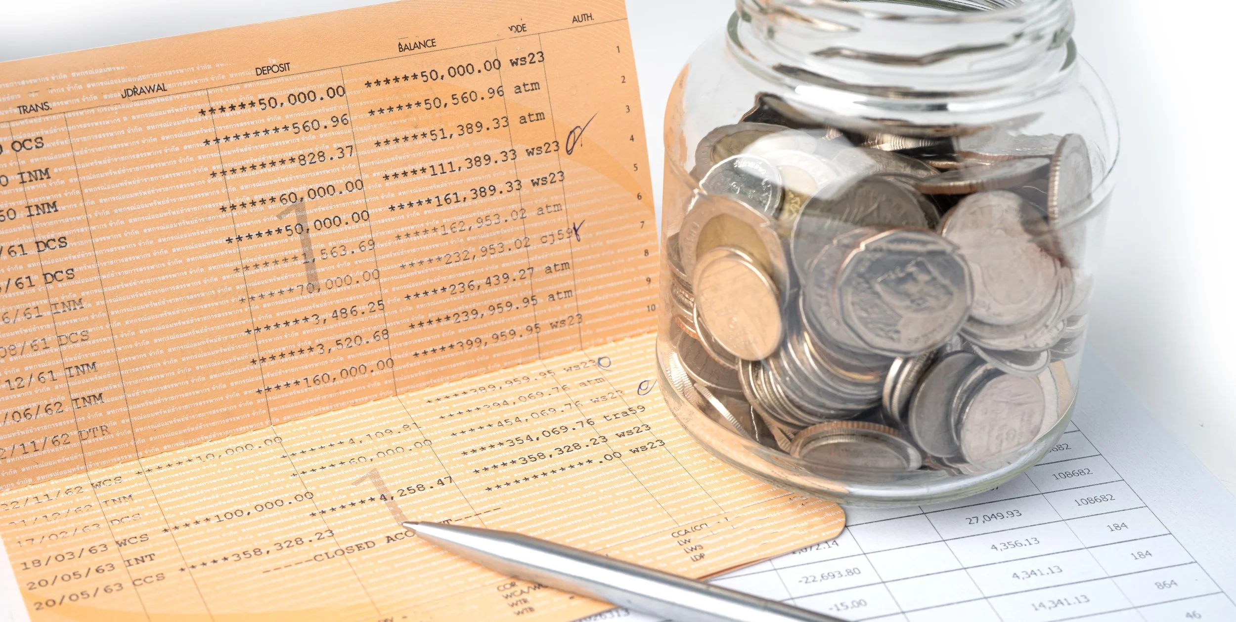 Bank statement and an open glass jar filled with coins on a table.