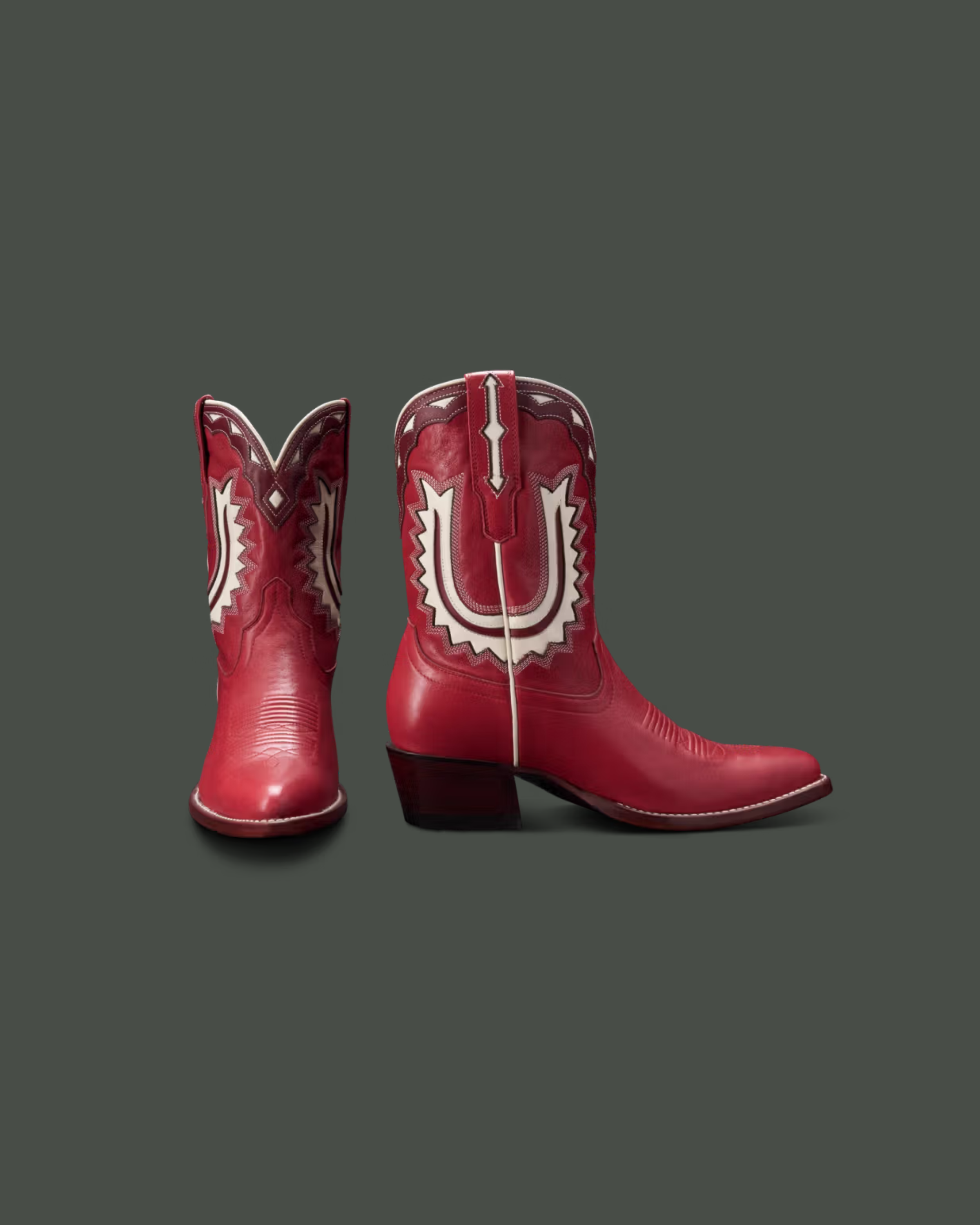 Pair of red cowboy boots with decorative white and black designs on a dark background.