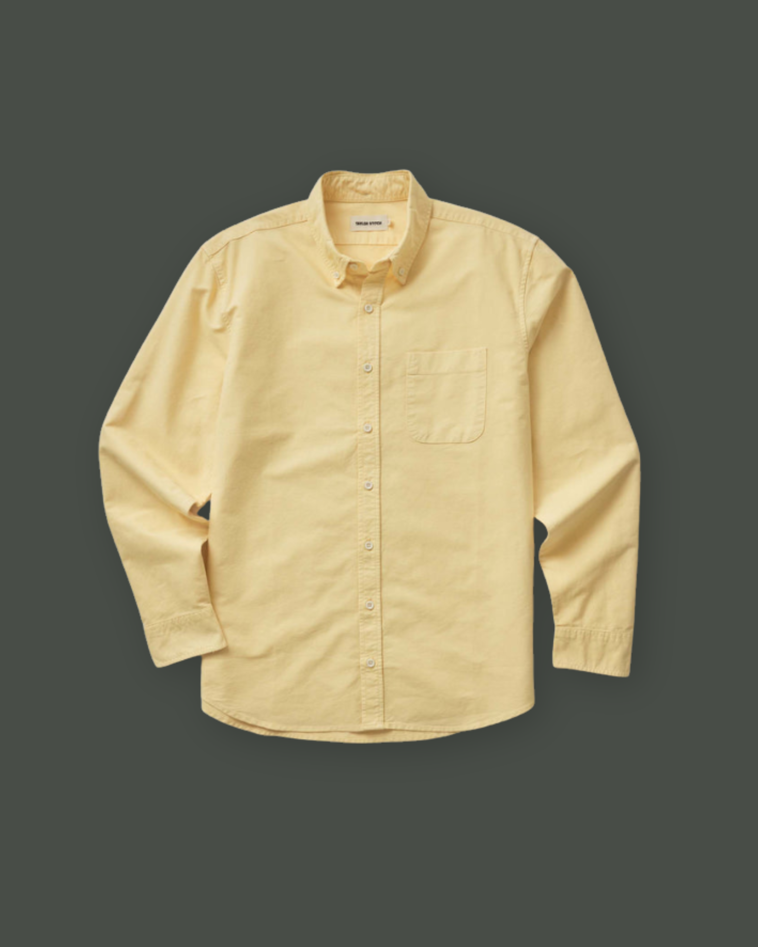 A light yellow button-up shirt with a pocket on the left chest, laid flat on a dark background.