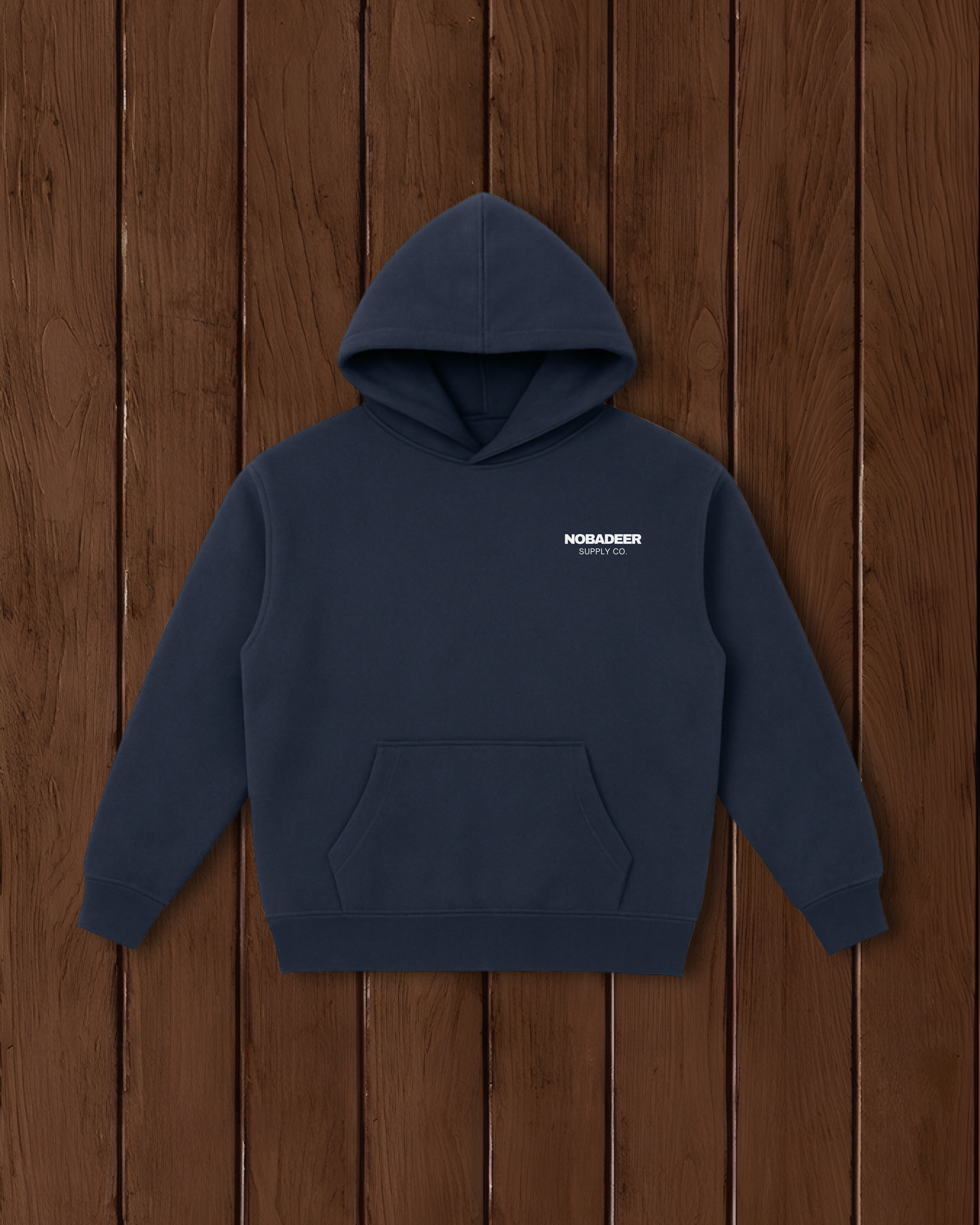 A navy blue hoodie with a front pocket and a small white logo reading 'NOBAFER SUPPLY CO.' on the chest, hanging against a wooden wall.
