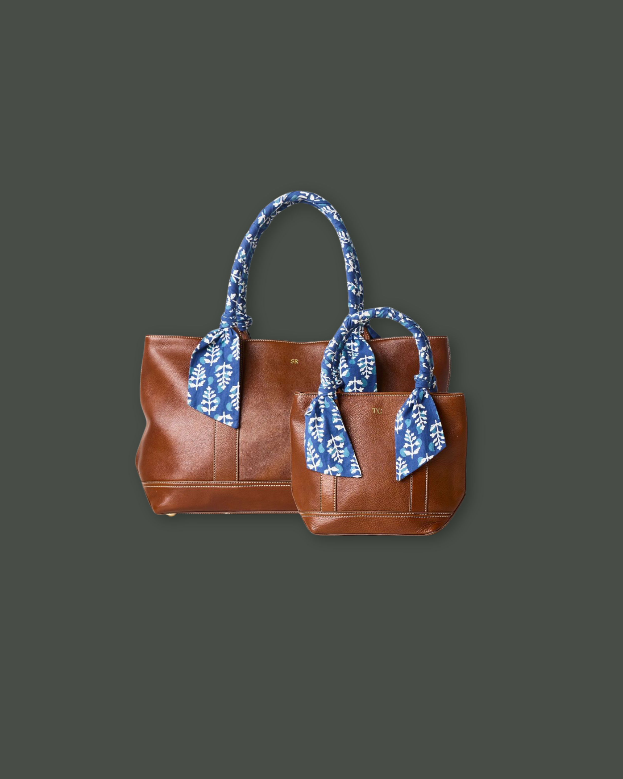Two brown leather tote bags with blue and white patterned scarves tied to the handles, placed against a dark gray background.