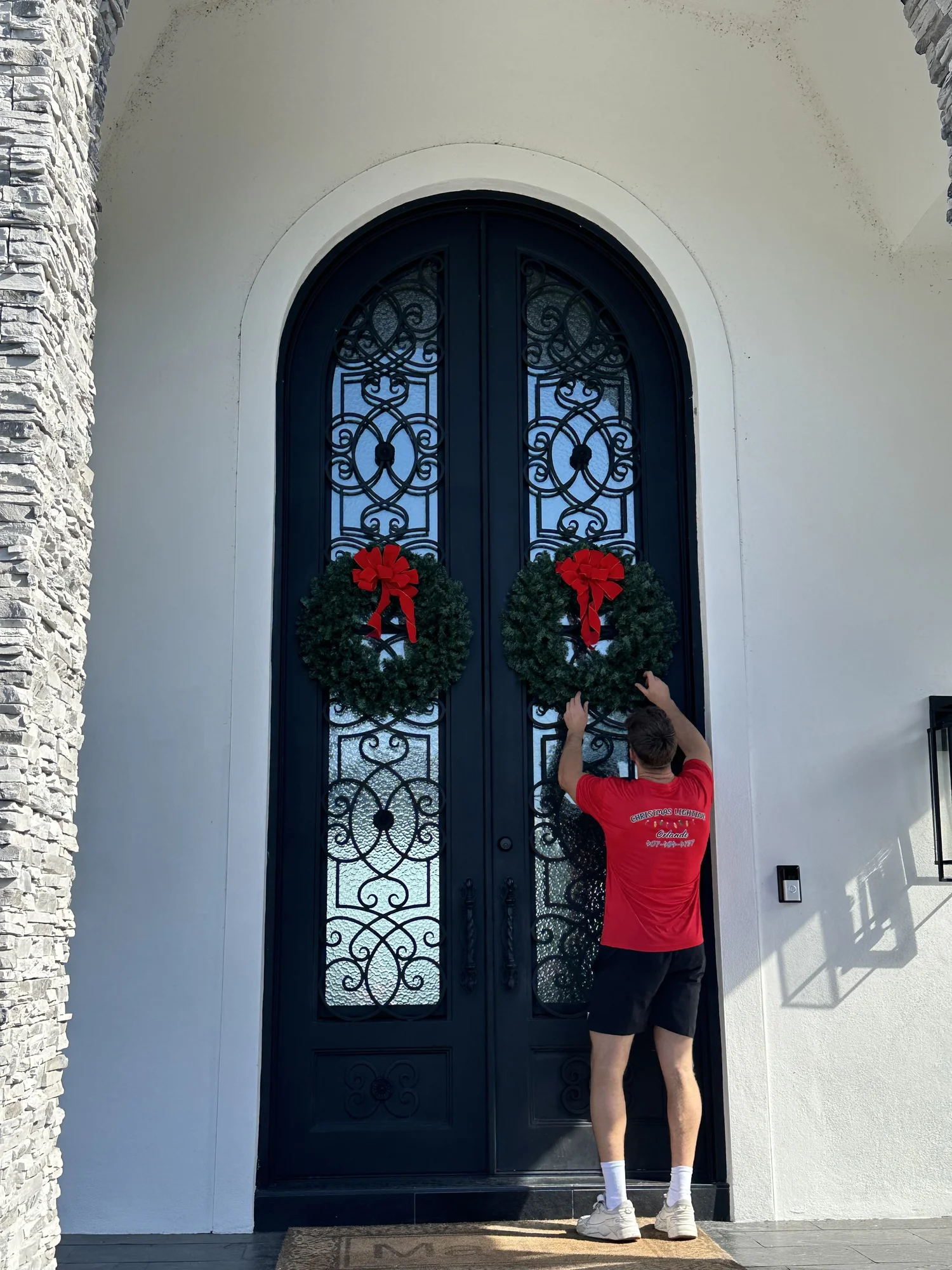 Holiday installer placing a red Christmas wreath on an elegant front door