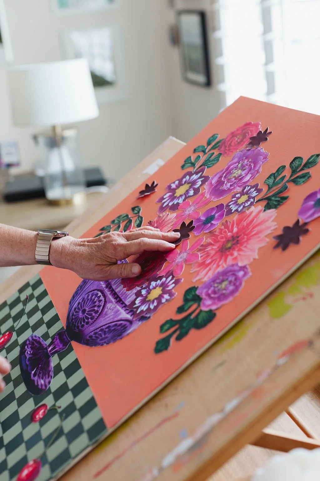 Artist Karey Bancroft creating a collage with various pink, purple, and yellow paper flowers on an orange background. (photo by Harmonie House Images)