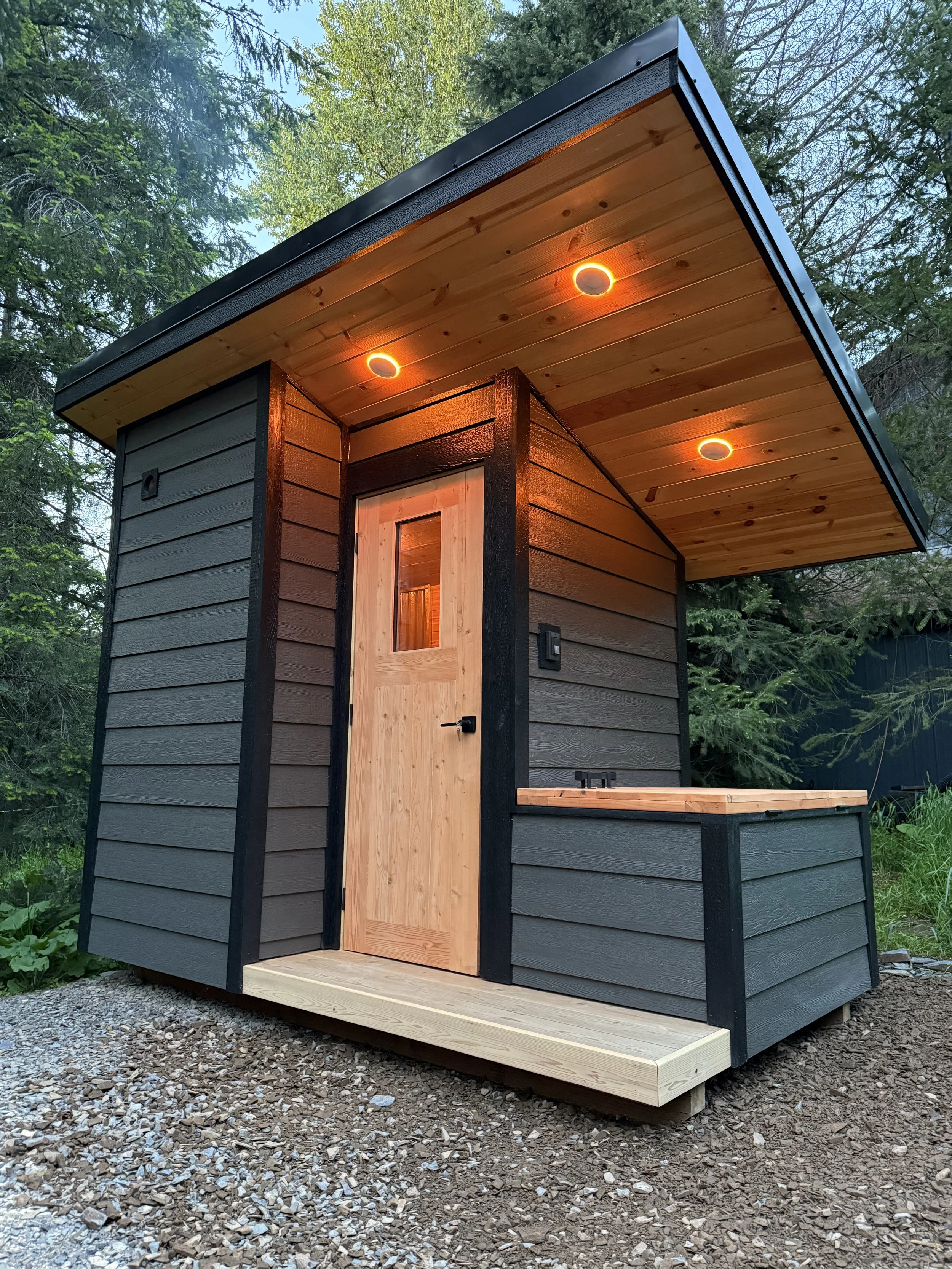 Custom rustic Sauna with cold plunge, built by CUB Saunas, featuring Gray siding, and black roofing and trim, with wood stove, in Stevensville, Montana