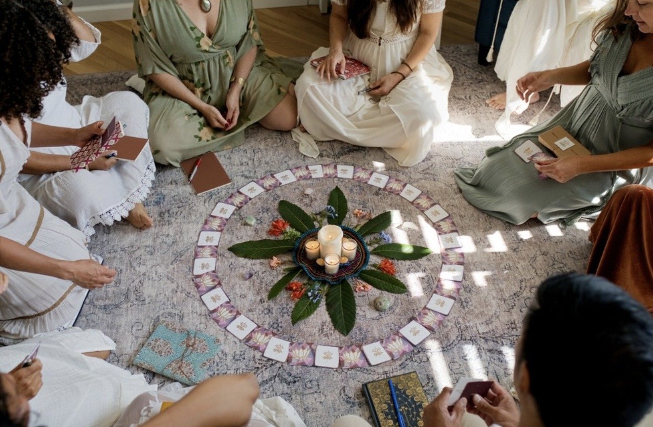 Group of people sitting in a circle around a decorated center with candles, surrounded by Insightful Reflection cards on the floor.