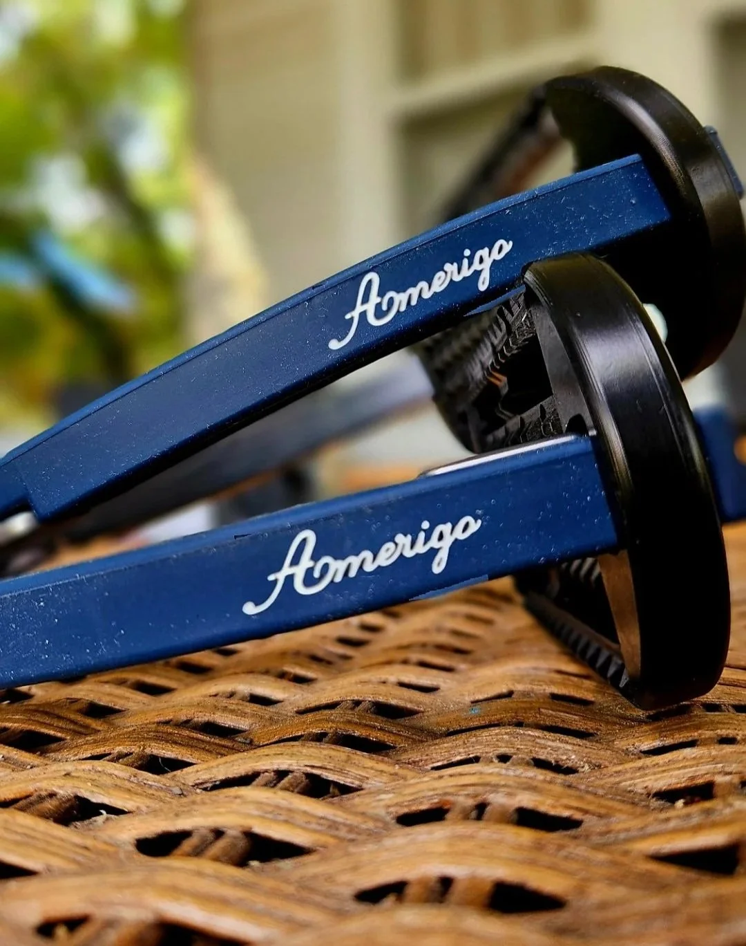 Close-up of navy Amerigo safety stirrups with black tread, resting on a wicker surface outdoors