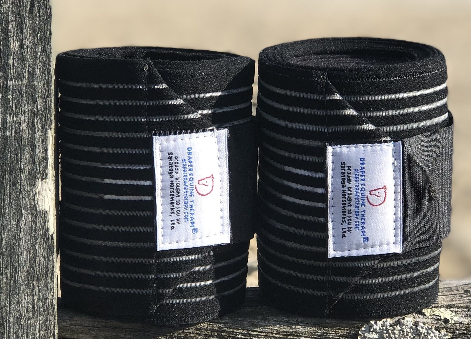 Draper Therapies Perfect Polo Wraps in black, rolled and displayed on a wooden fence in natural light.