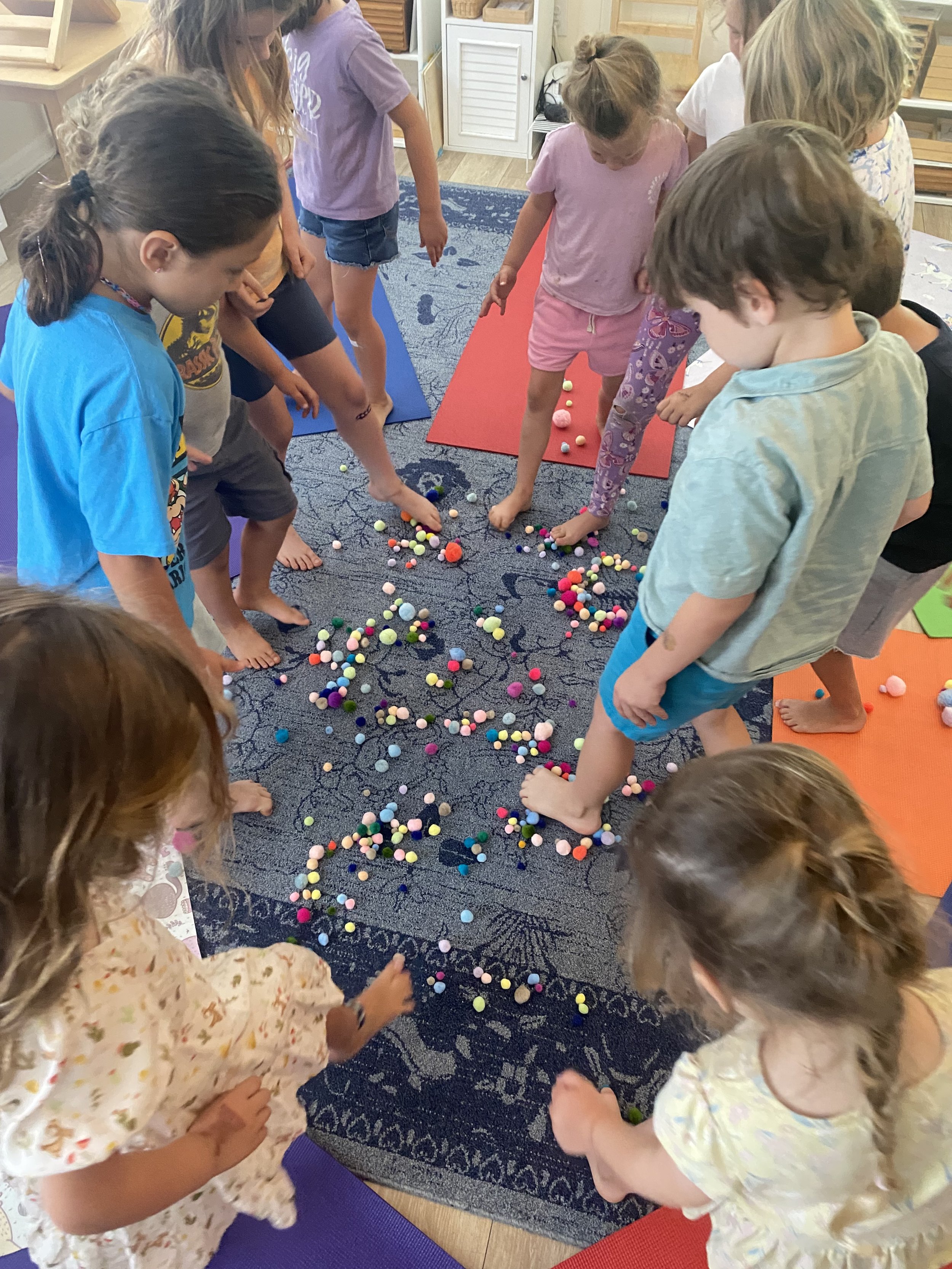 Group of children playing a game with colorful pom-poms on the floor.