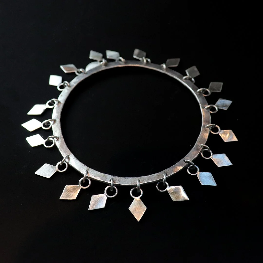 Handmade sterling silver bangle featuring articulated diamond-shaped charms