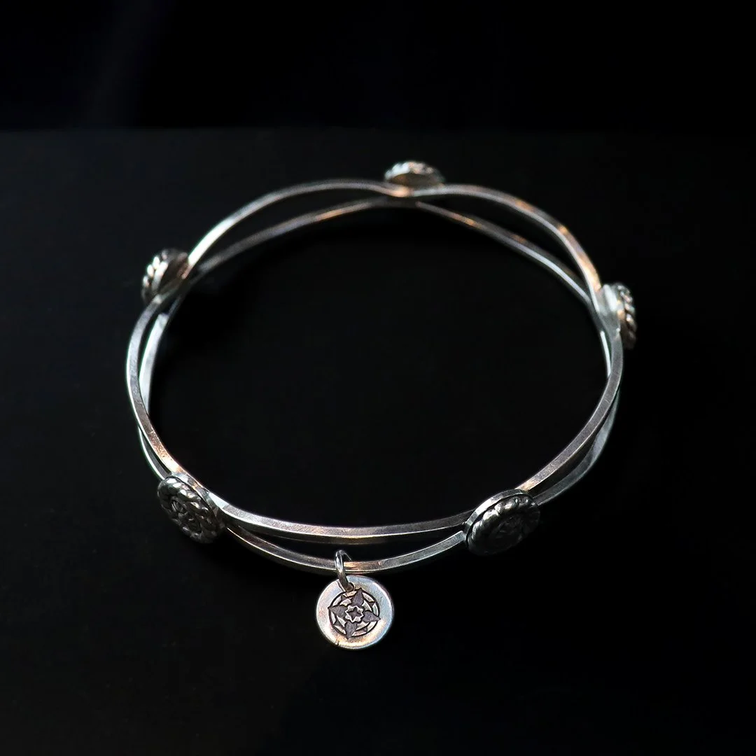 Handcrafted silver bangle featuring sculpted medallion accents