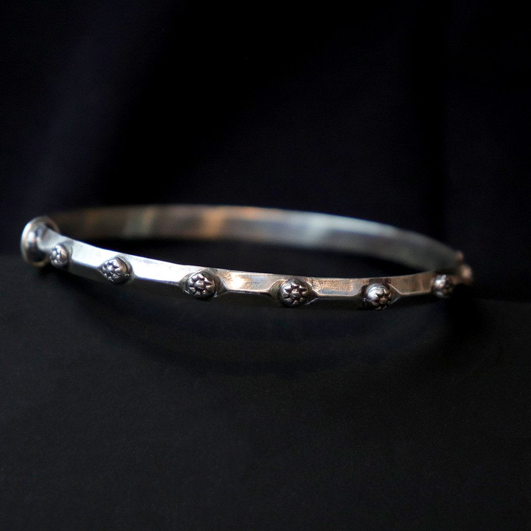 Handmade sterling silver bangle with small raised floral motifs spaced evenly along the band