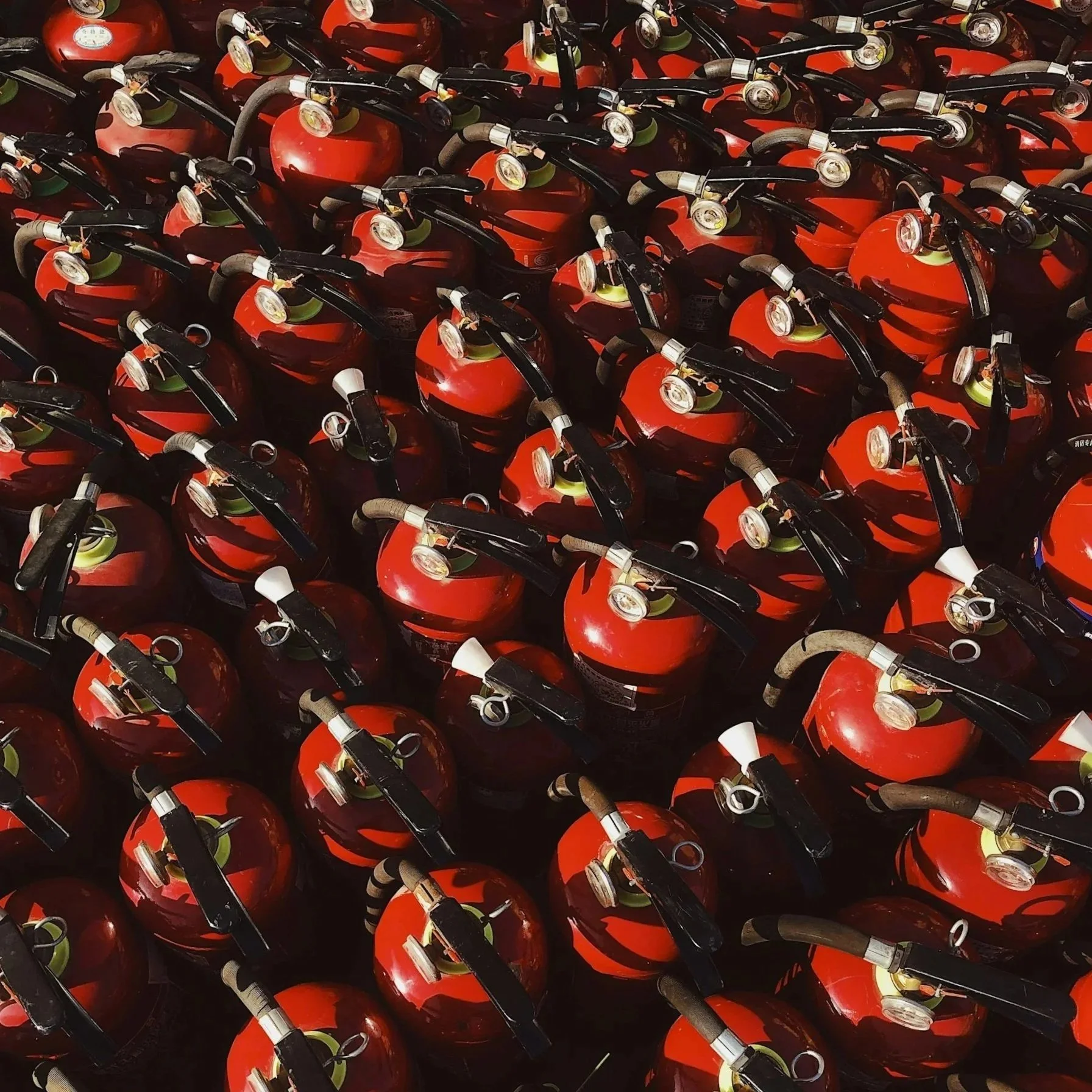 Multiple red fire extinguishers arranged closely together.