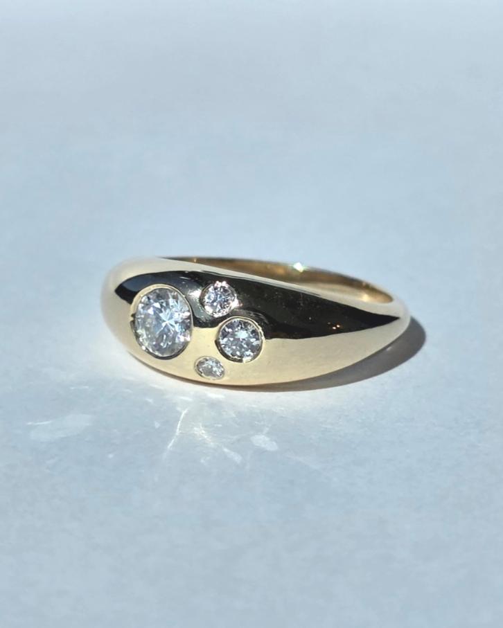 Gold ring with five diamonds of varying sizes, arranged in a decorative pattern.