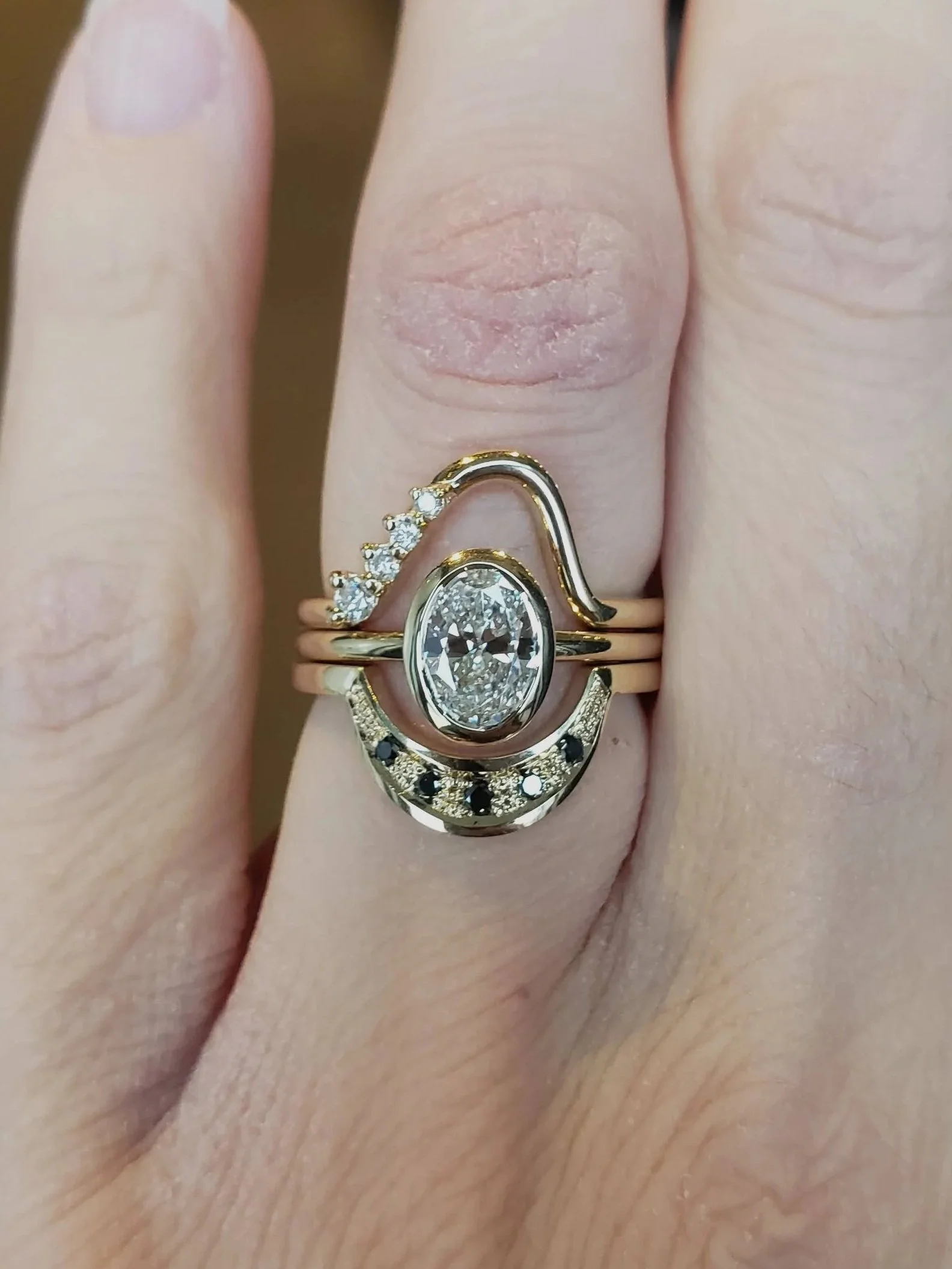 Custom wedding set in 14k yellow gold, centre is an oval brilliant cut diamond in a bezel setting, below band showcases balck diamonds gypsy set into textured gold, above band features white diamonds.