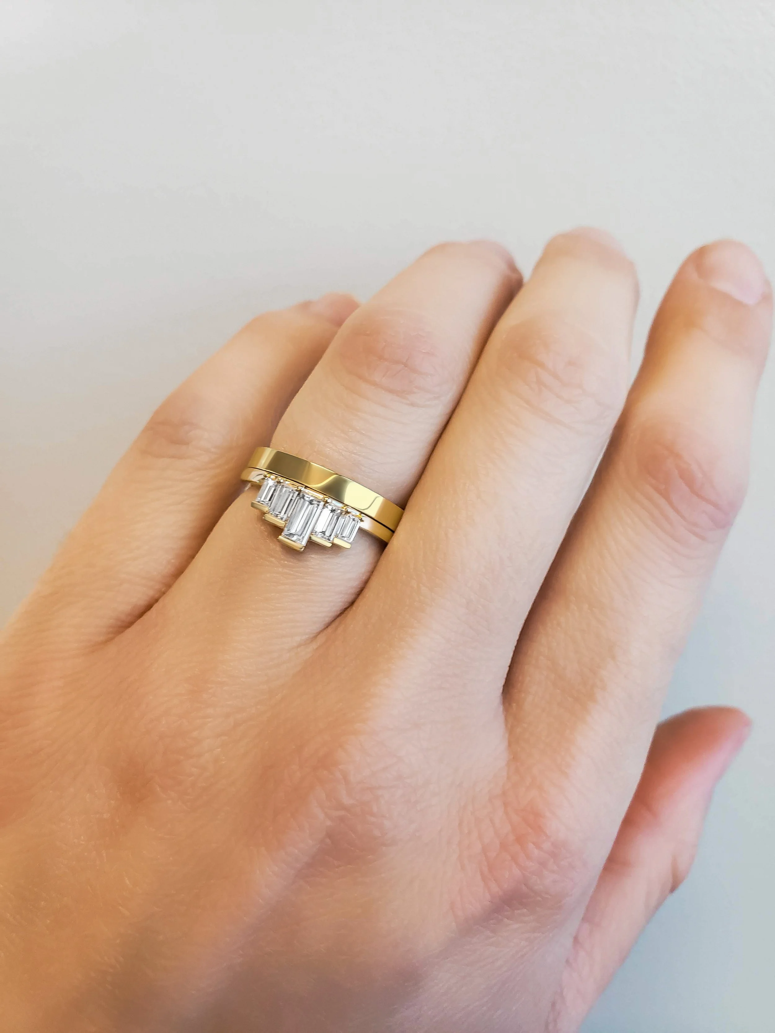 Close-up of a hand wearing a gold ring with a row of baguette-cut diamonds.