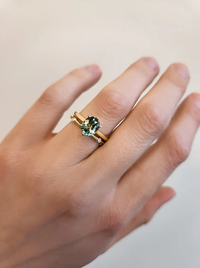 A hand displaying a gold ring with a large oval green gemstone and small side stones.
