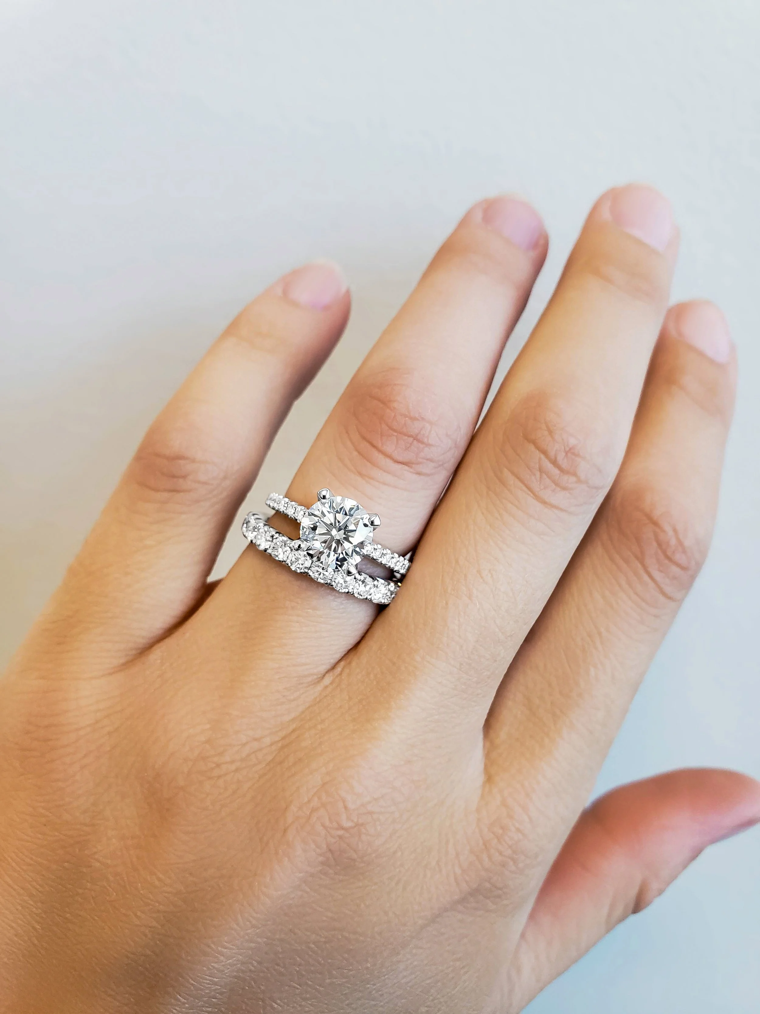 Close-up of a hand displaying an engagement ring with a large central diamond and a wedding band with smaller diamonds.
