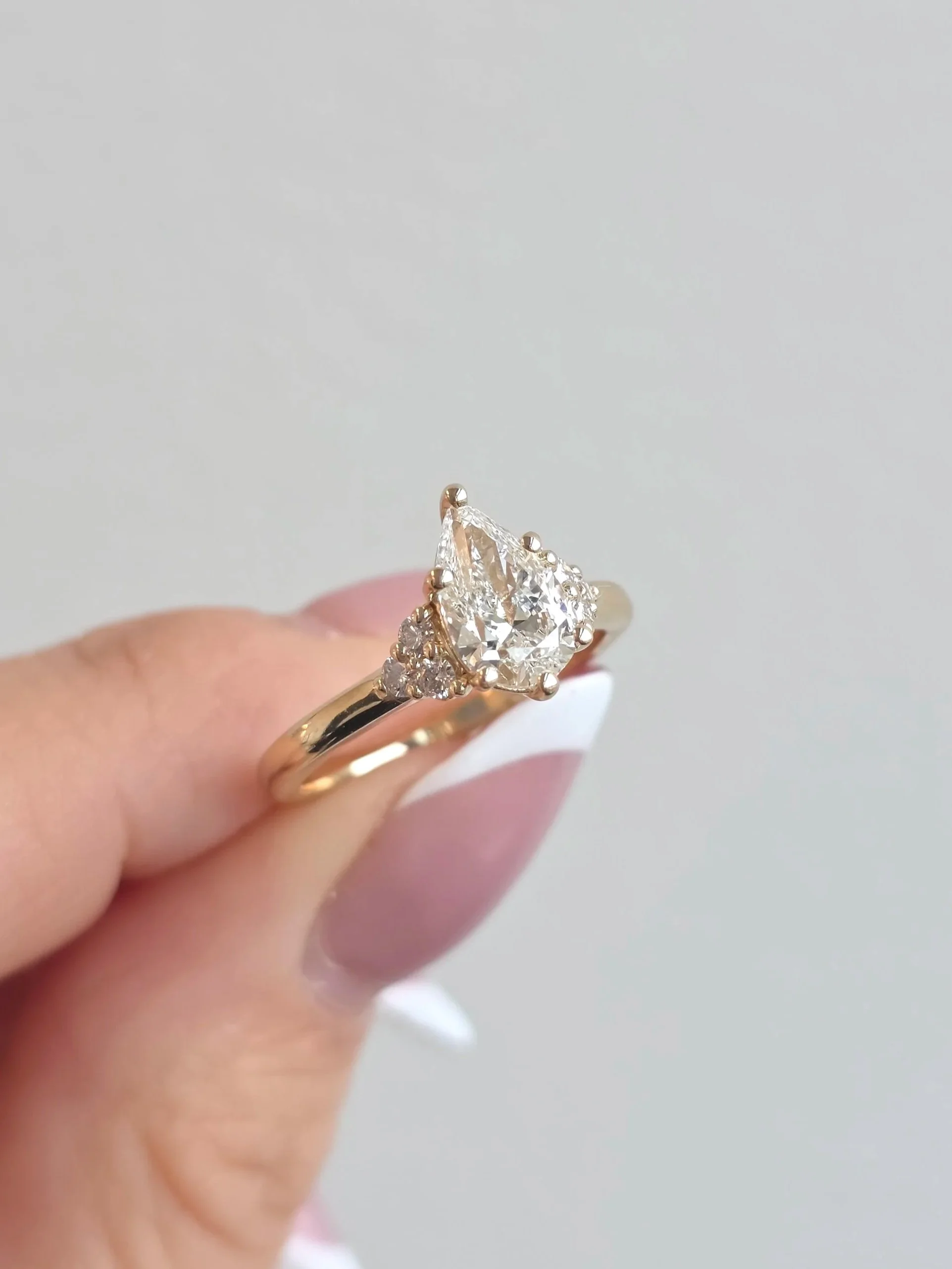 A person's hand holding a gold ring with a large, pear-shaped diamond surrounded by smaller diamonds set in a prong setting.