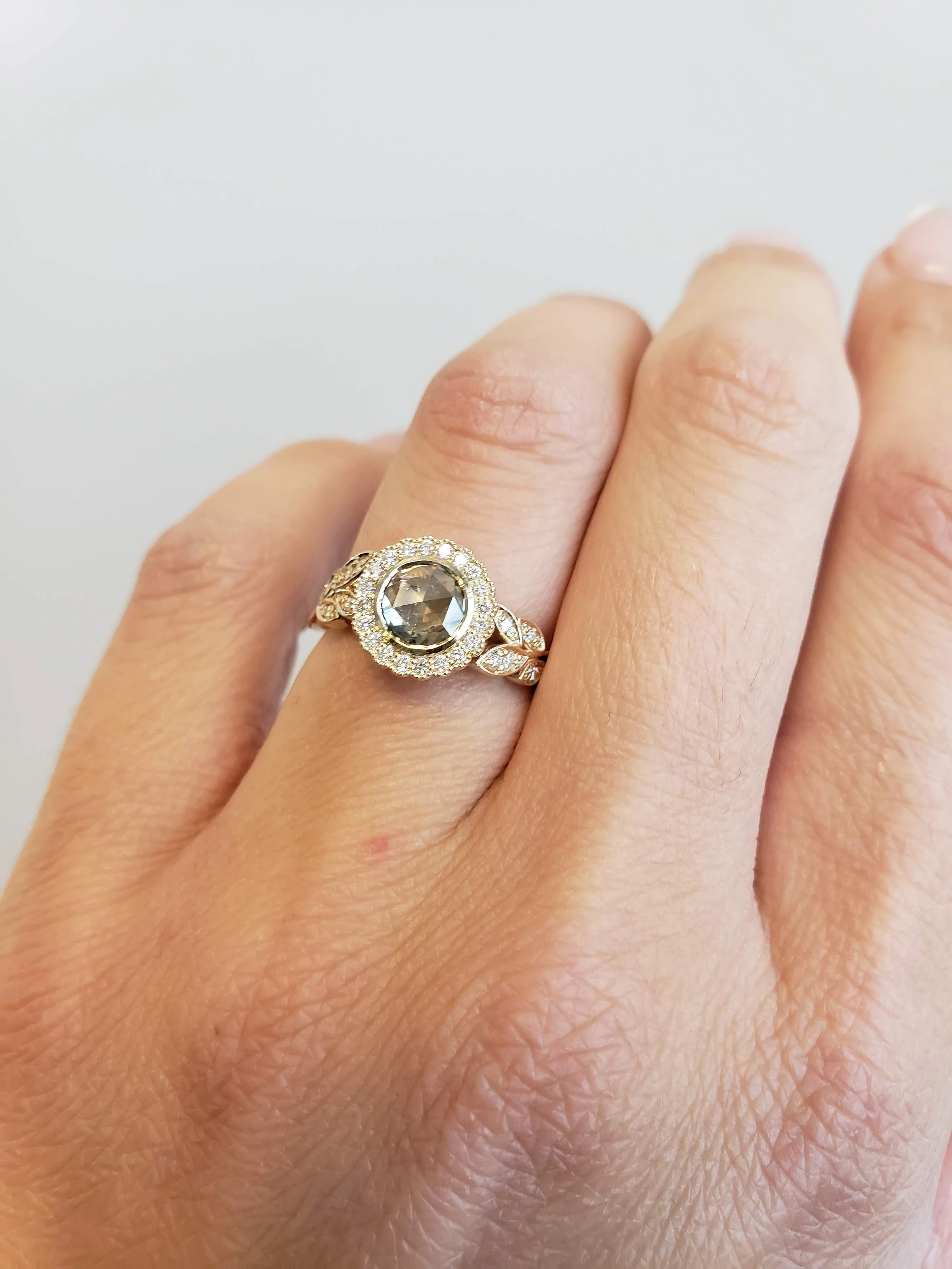 Custom floral motif engagement ring with rose cut salt and pepper centre set into milgrain bezel, with prong set diamond accents in yellow gold