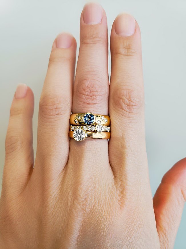 Bezel set custom yellow gold ring set into wide bands with gypsy set accent diamonds