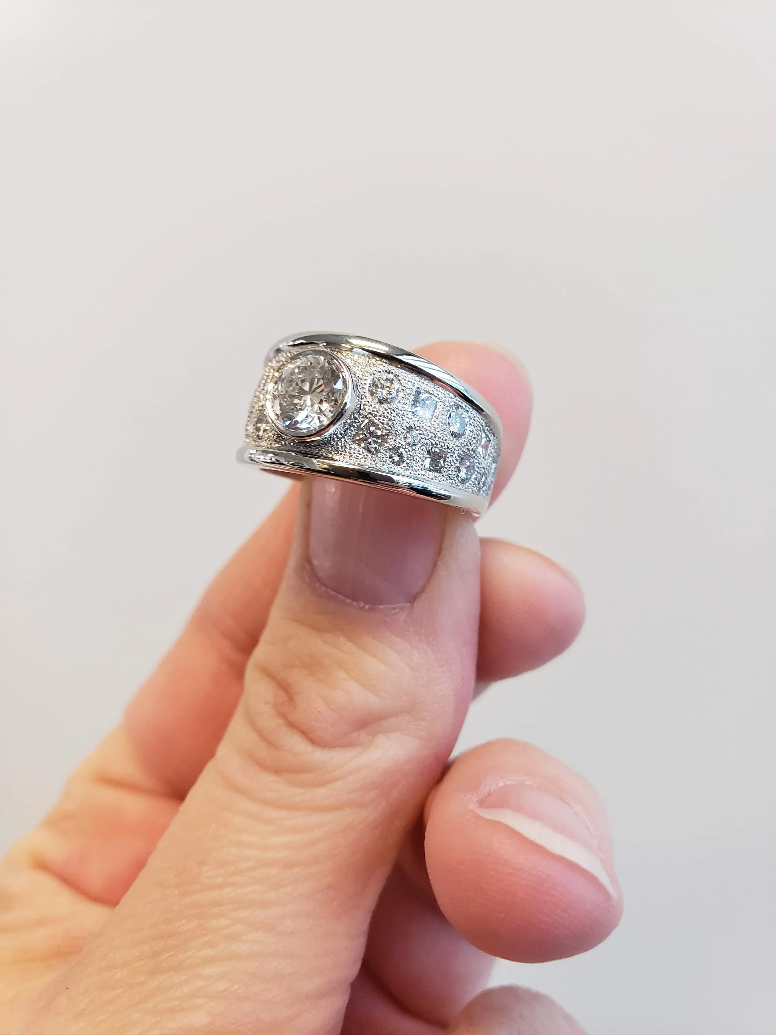 Round brilliant cut diamond ring with gypsy set accent diamonds, set into white gold with textured finish