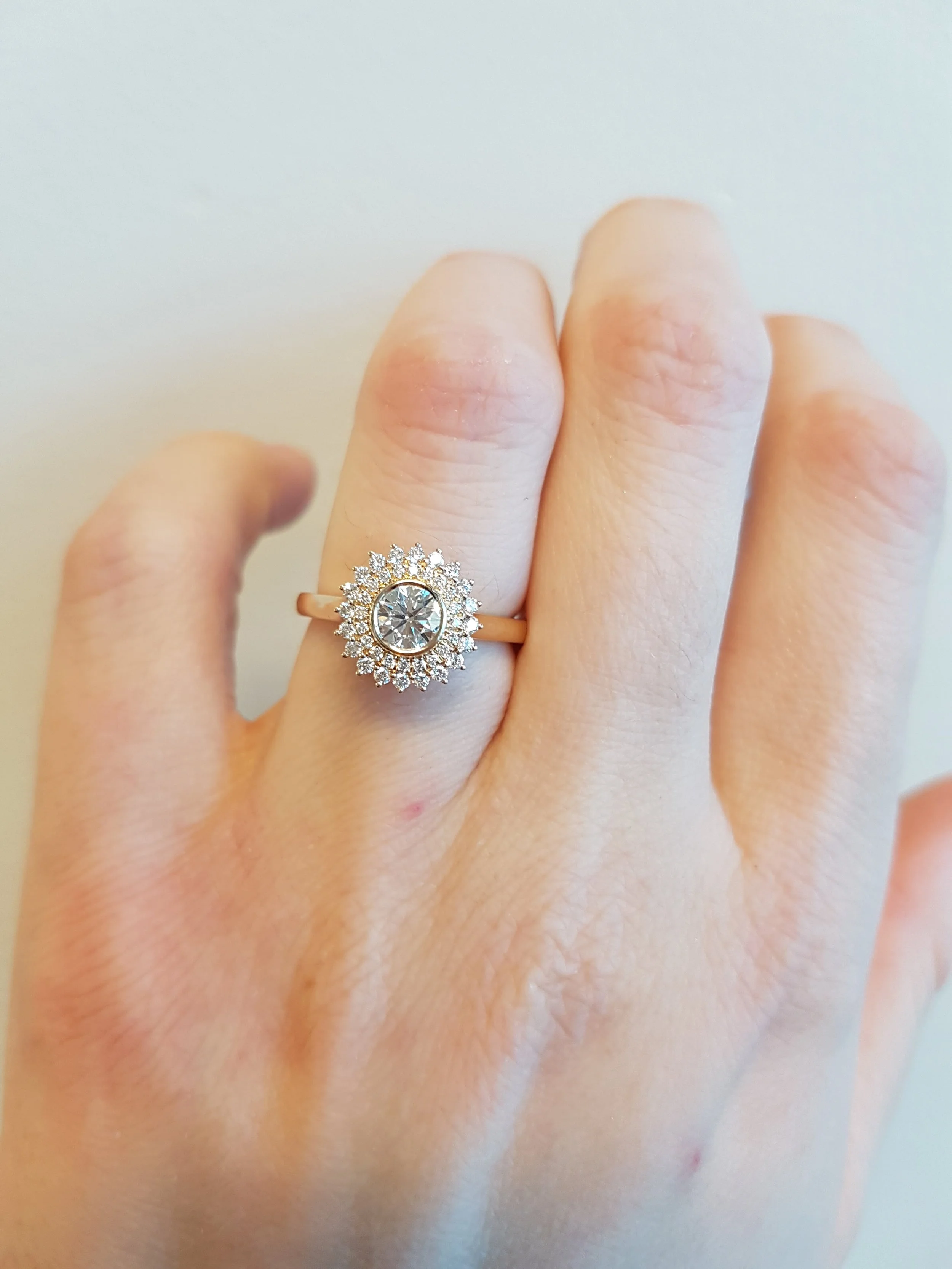 Round brilliant cut diamond bezel set into double halo engagement ring, 14K rose gold.