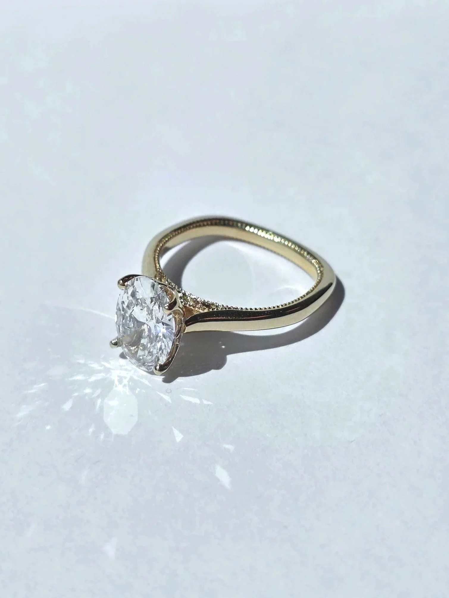 A gold ring with a large, oval-cut diamond solitaire setting on a white surface.