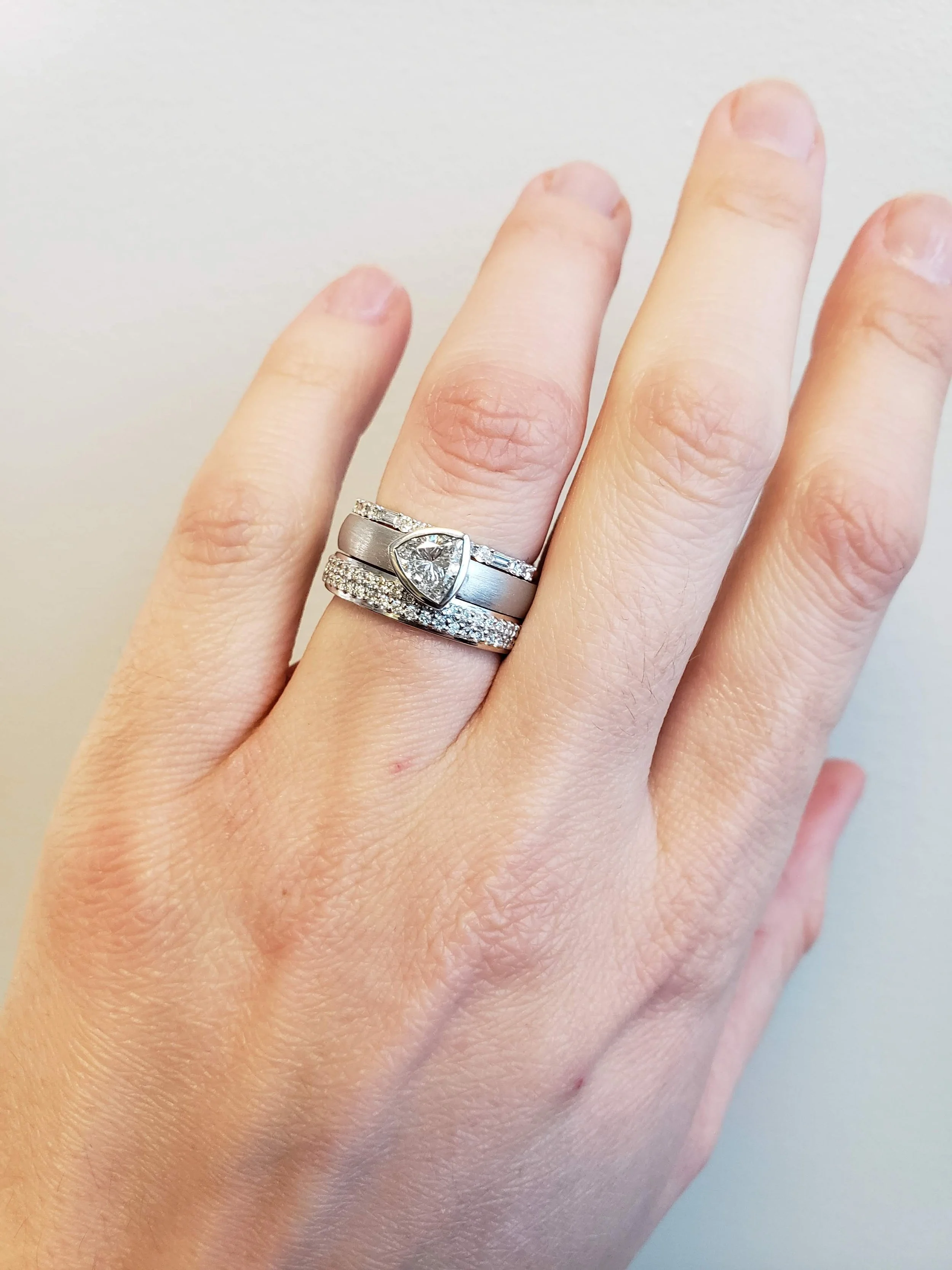 Trillon cut diamond bezel set into 19K white gold, pave and micro pave bands on either side