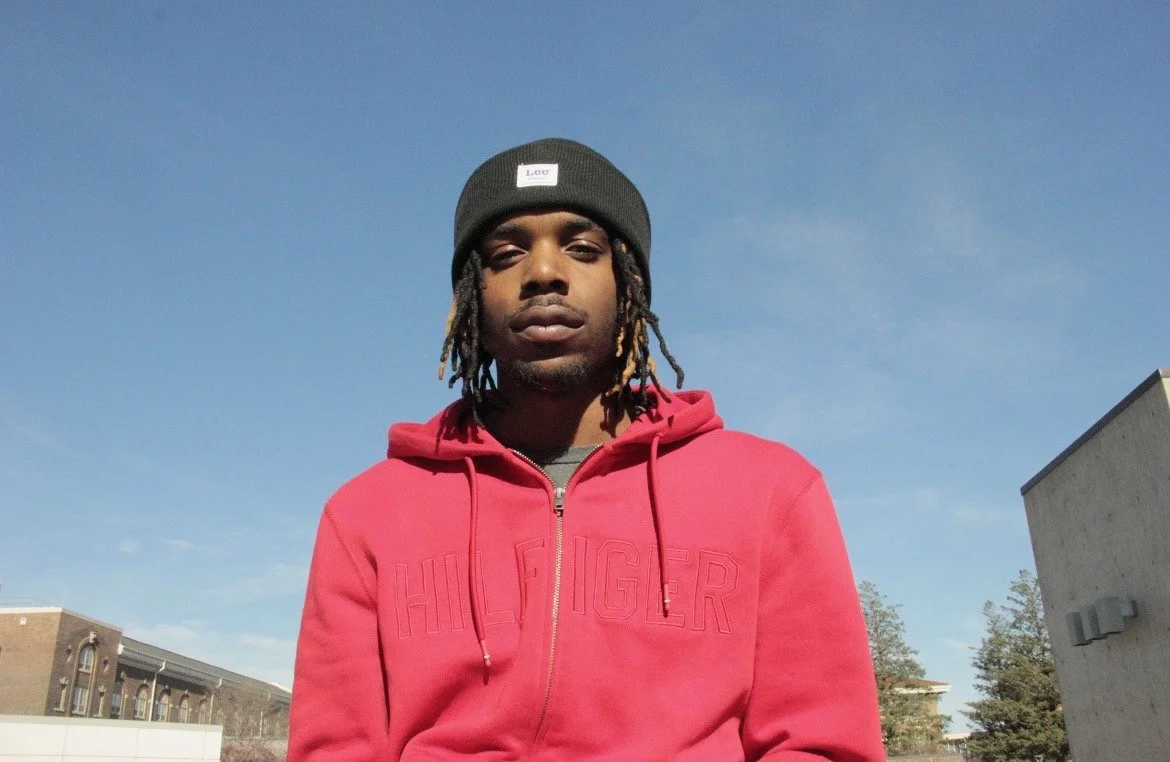 Young man wearing a black beanie and red hoodie with 'HILFIGER' logo, standing outdoors against a clear blue sky.