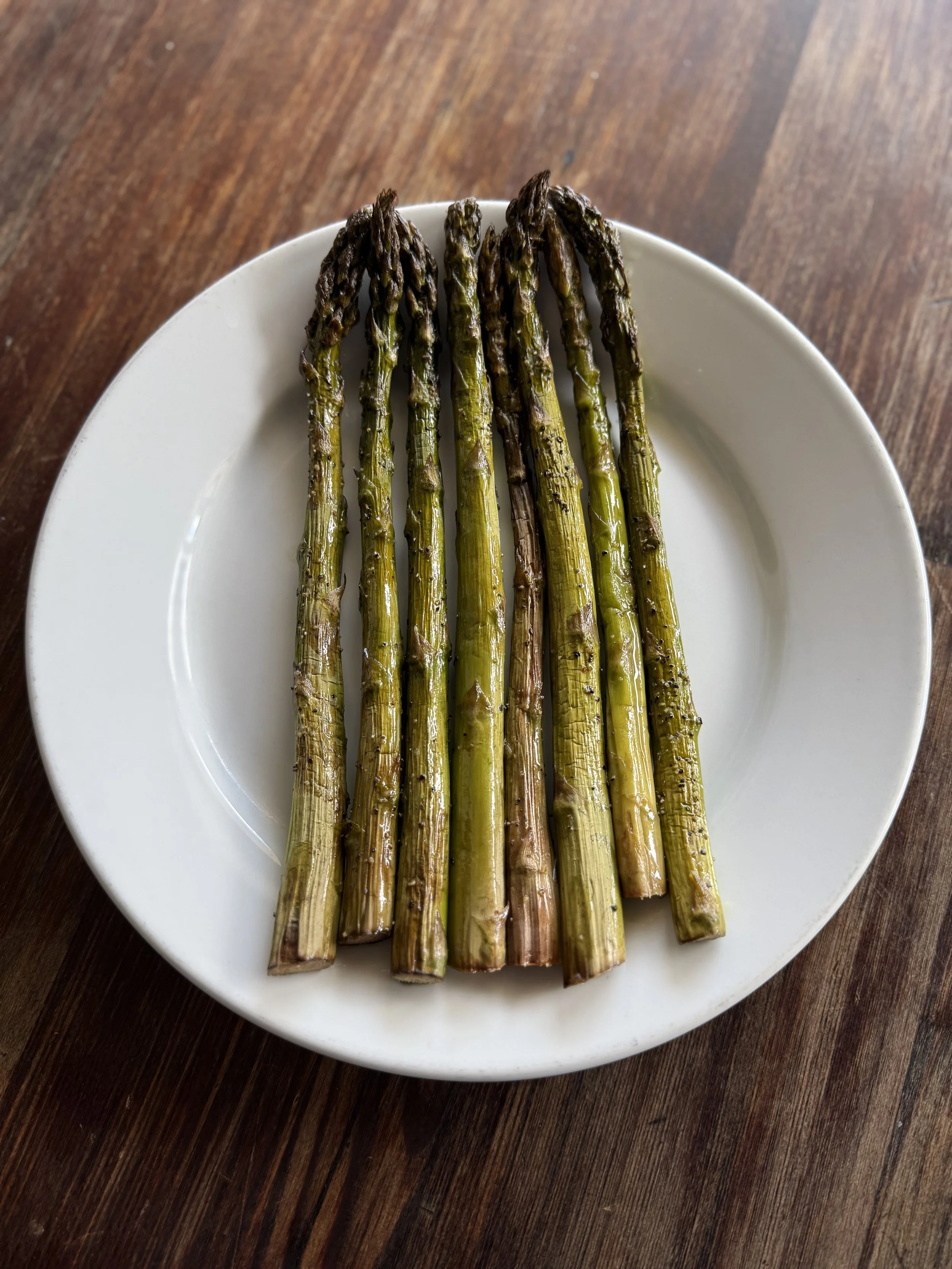 Grilled asparagus on a white plate on a wooden surface.