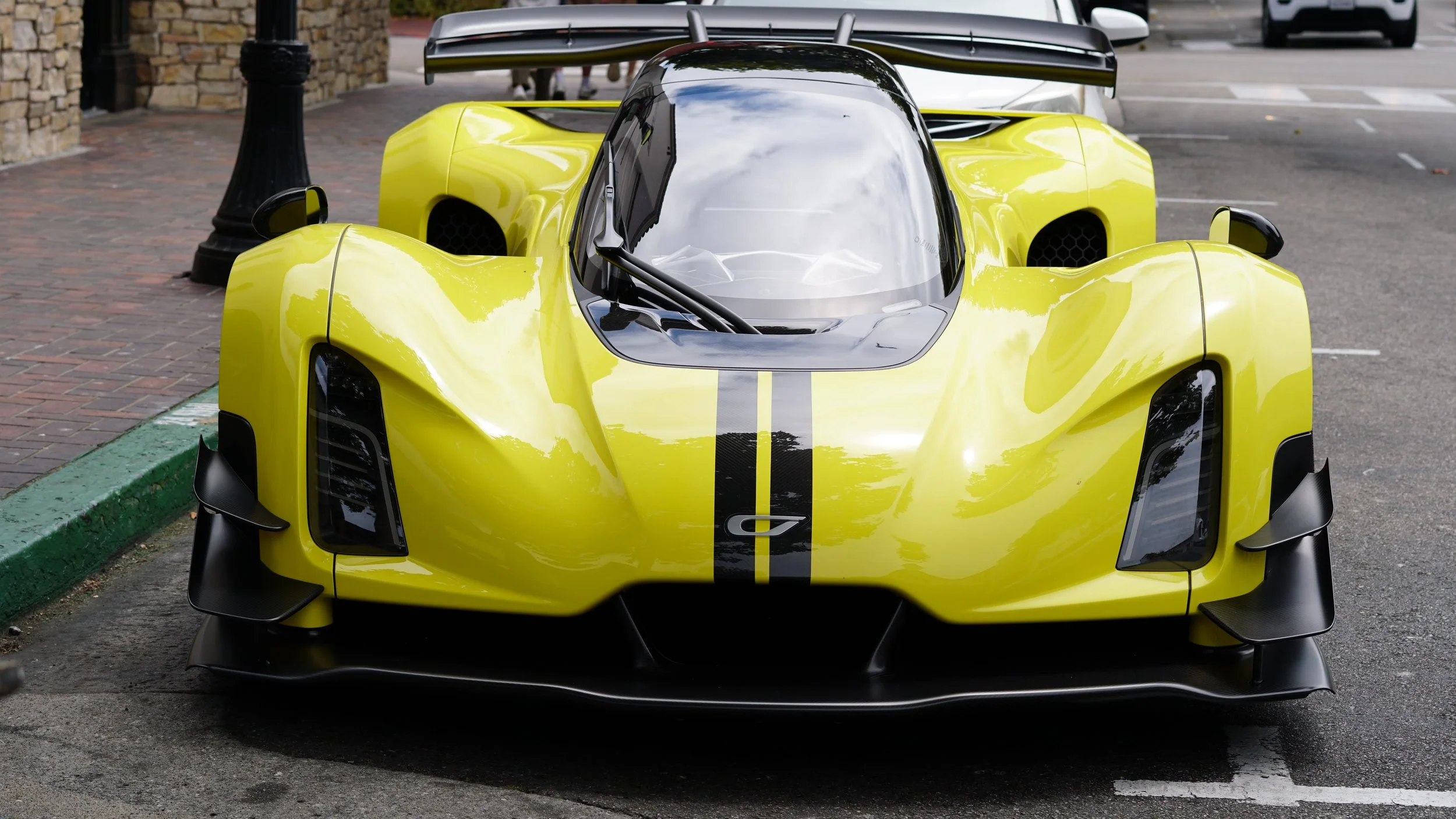 Front view of a bright yellow racing car with black racing stripes, parked in a parking lot.