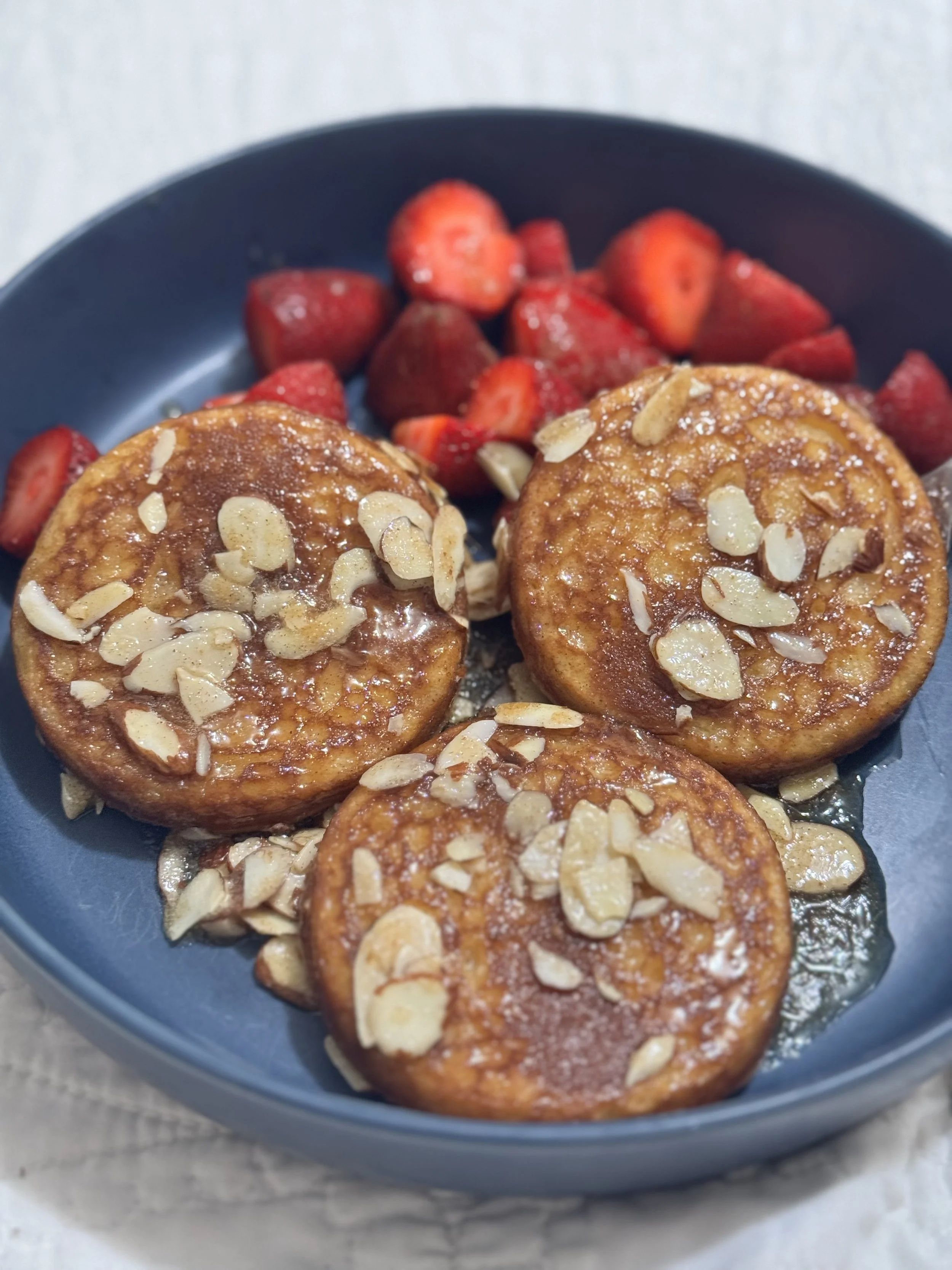 A bowl with three caramelized banana slices topped with almonds, served with sliced strawberries.
