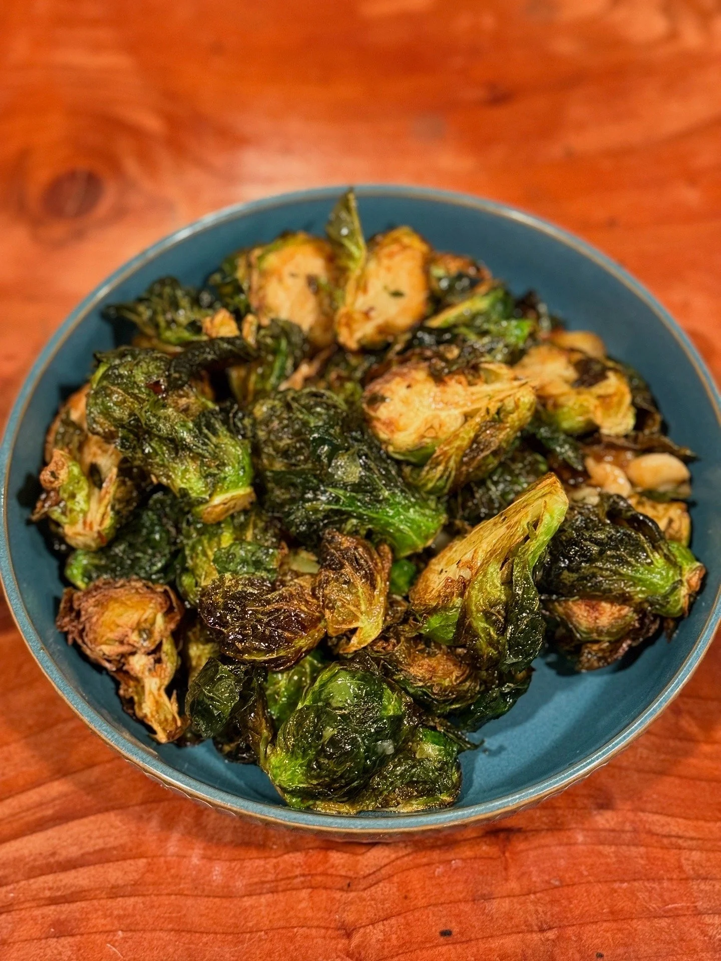 A bowl of roasted Brussels sprouts on a wooden table.