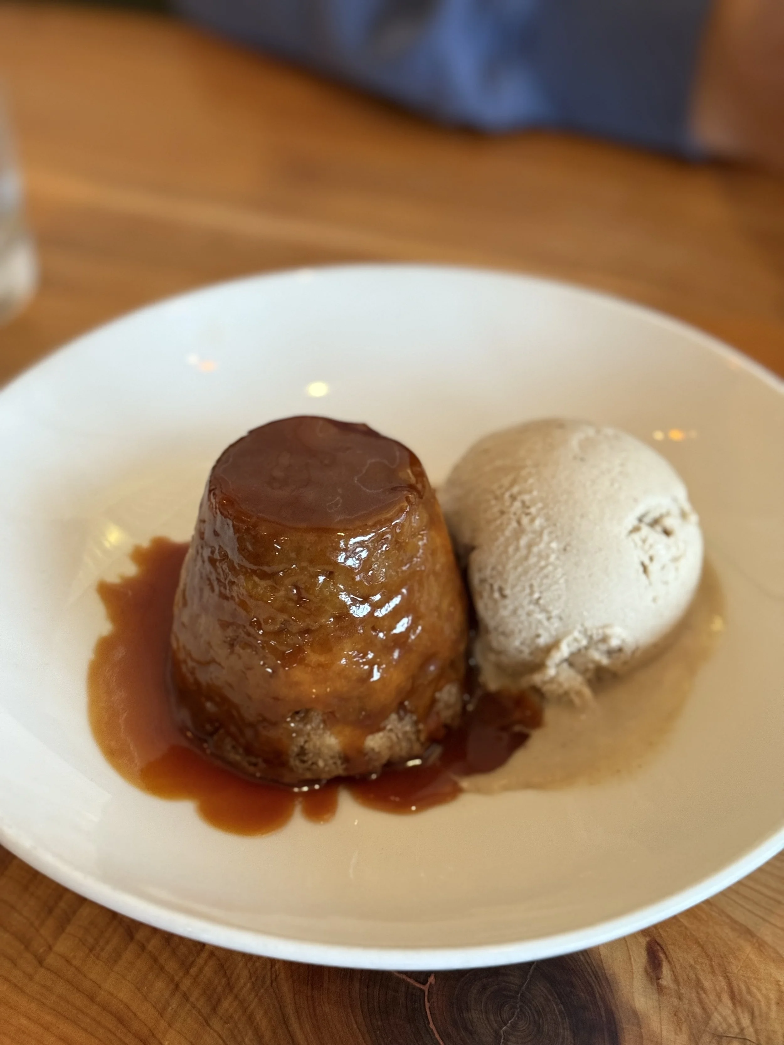 Sweet caramel flan with a scoop of ice cream on a white plate.