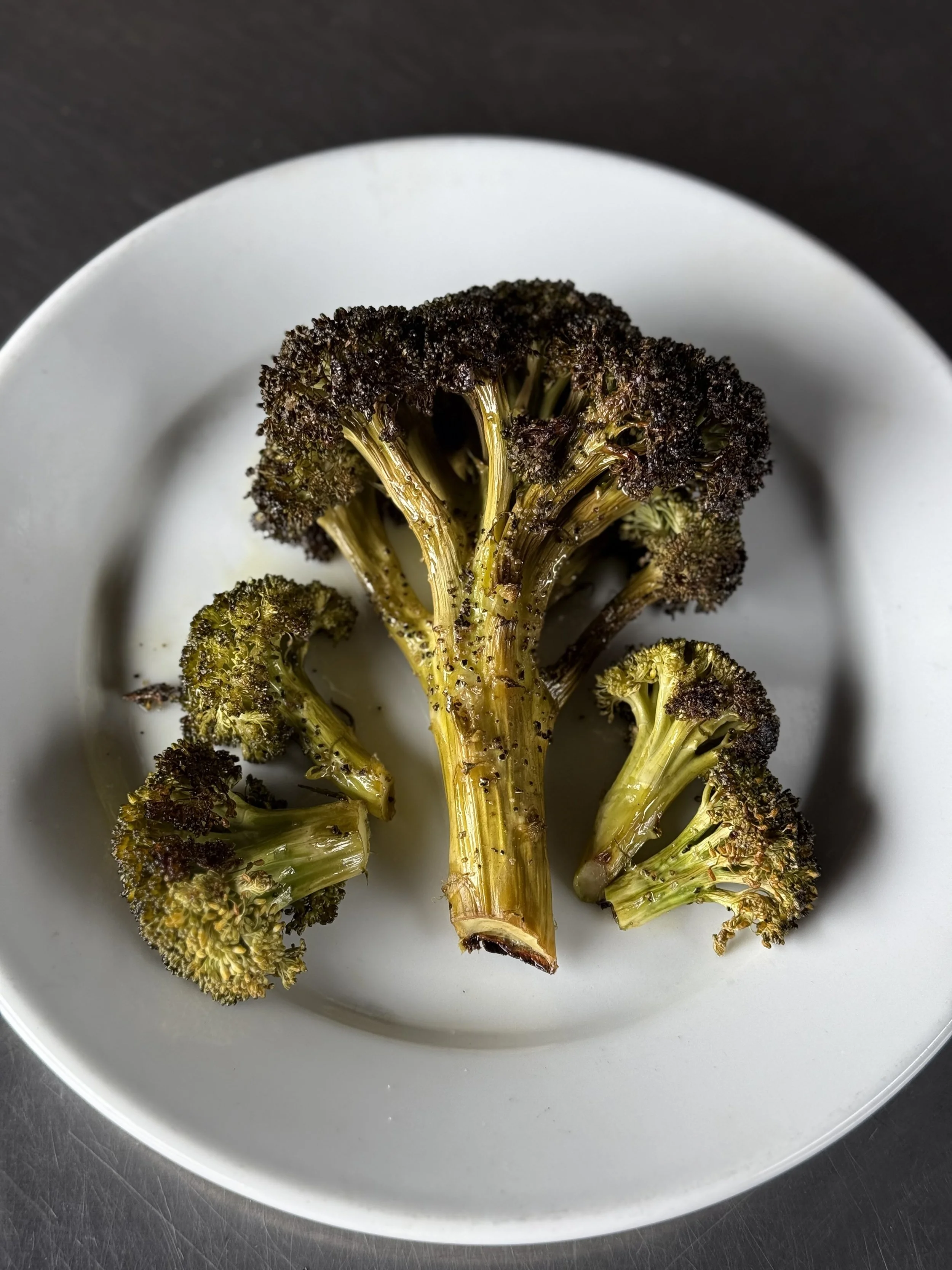 Charred broccoli florets on a white plate.