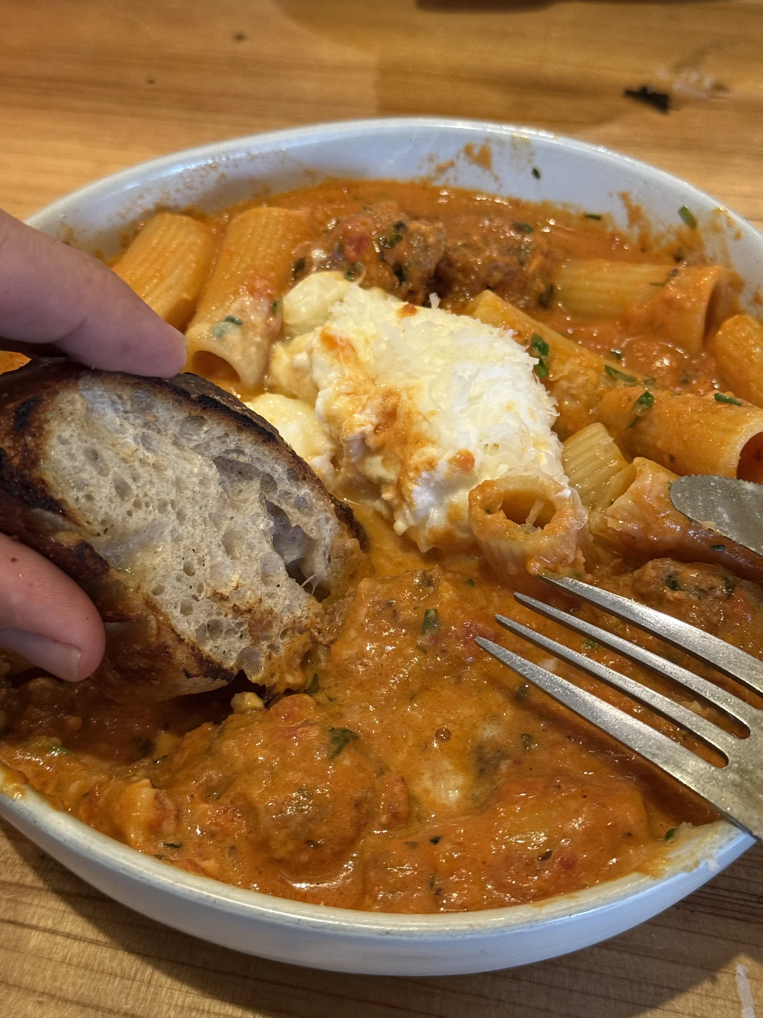 A bowl of baked ziti pasta with marinara sauce, topped with cheese, served with a piece of toasted bread