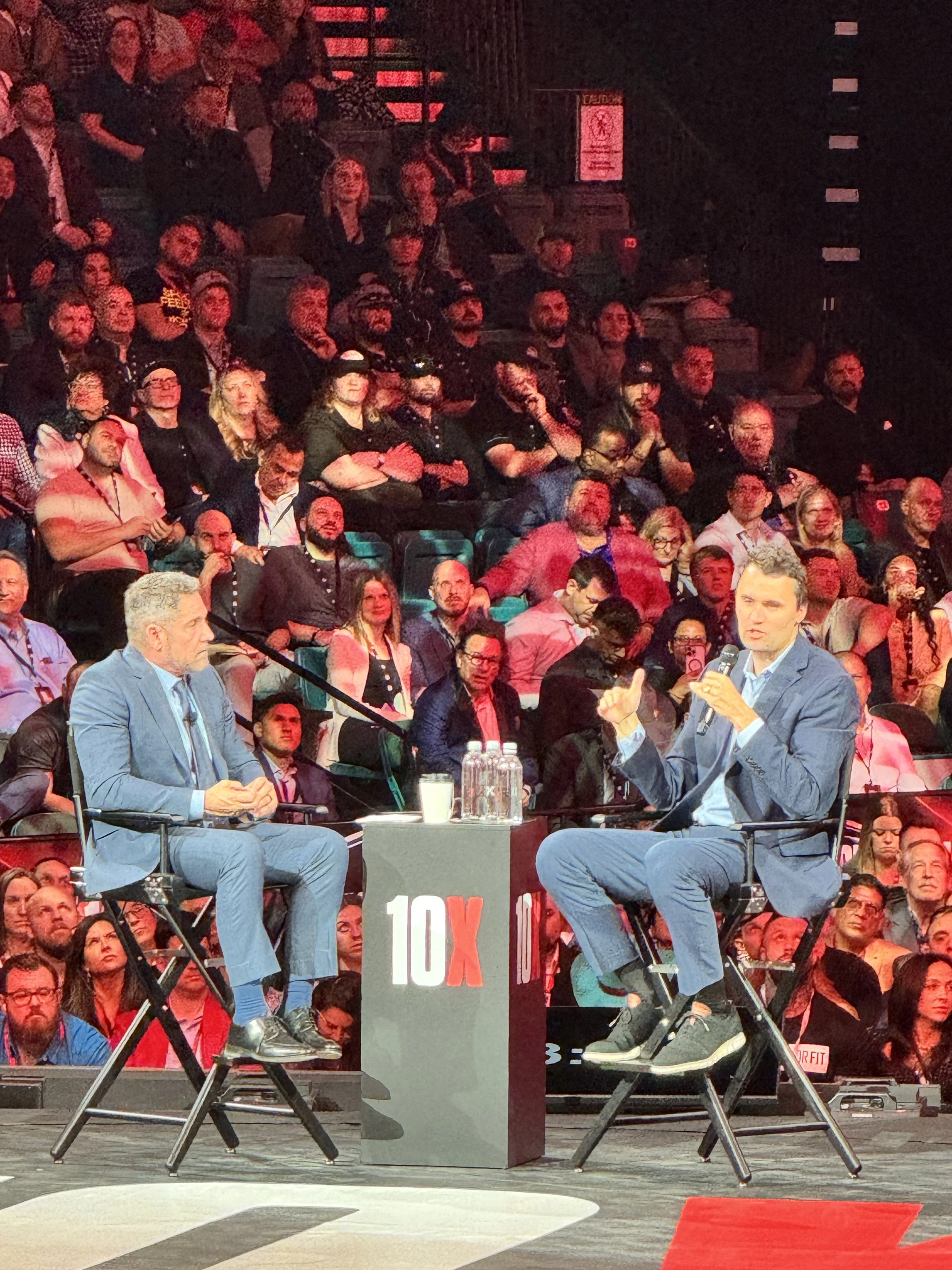 Two men sitting on stage in conversation during a TEDx event, with a seated audience watching.
