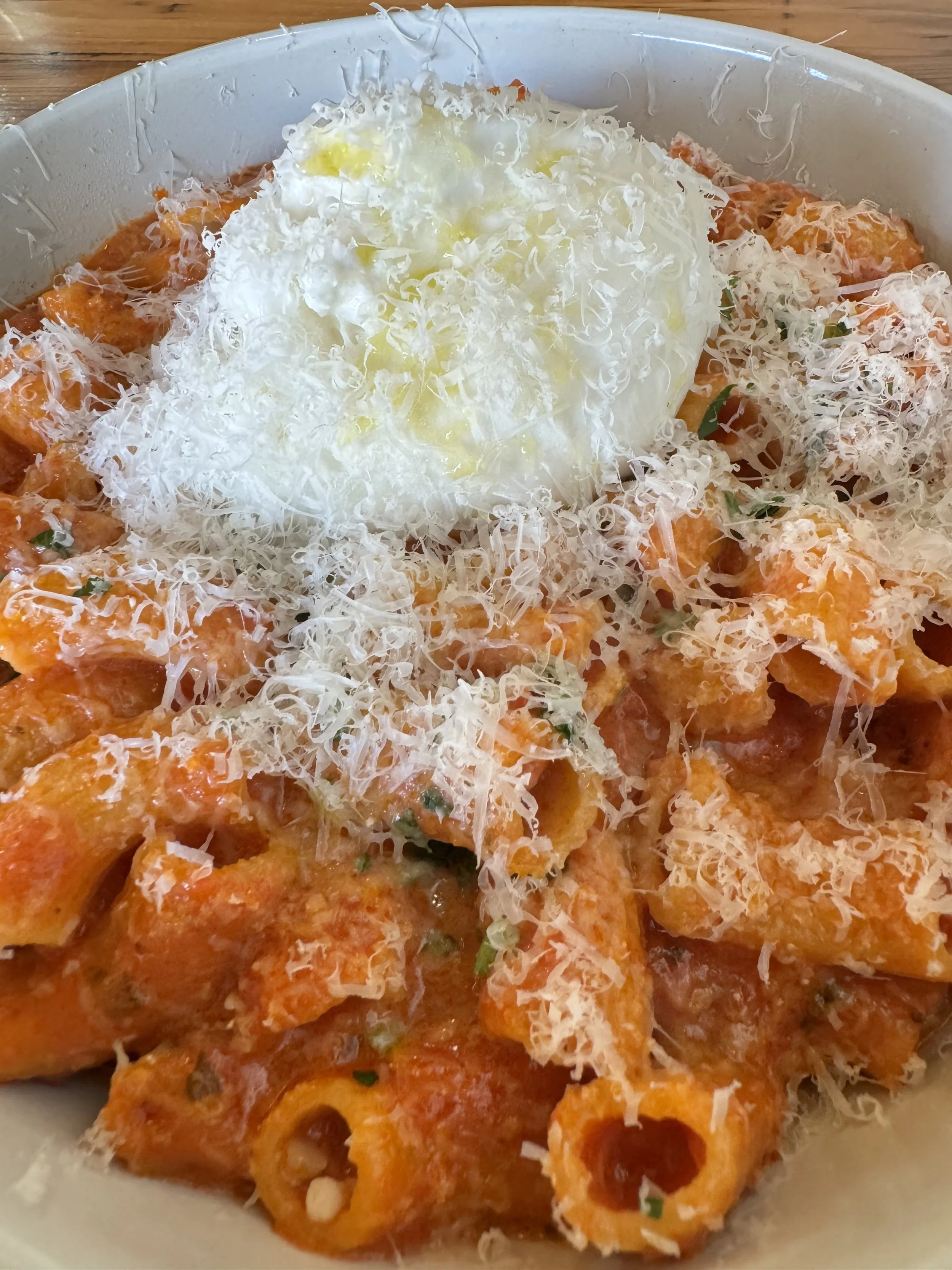Bowl of baked pasta with marinara sauce, topped with grated cheese, a dollop of sour cream or ricotta, and sprinkled with chopped herbs.