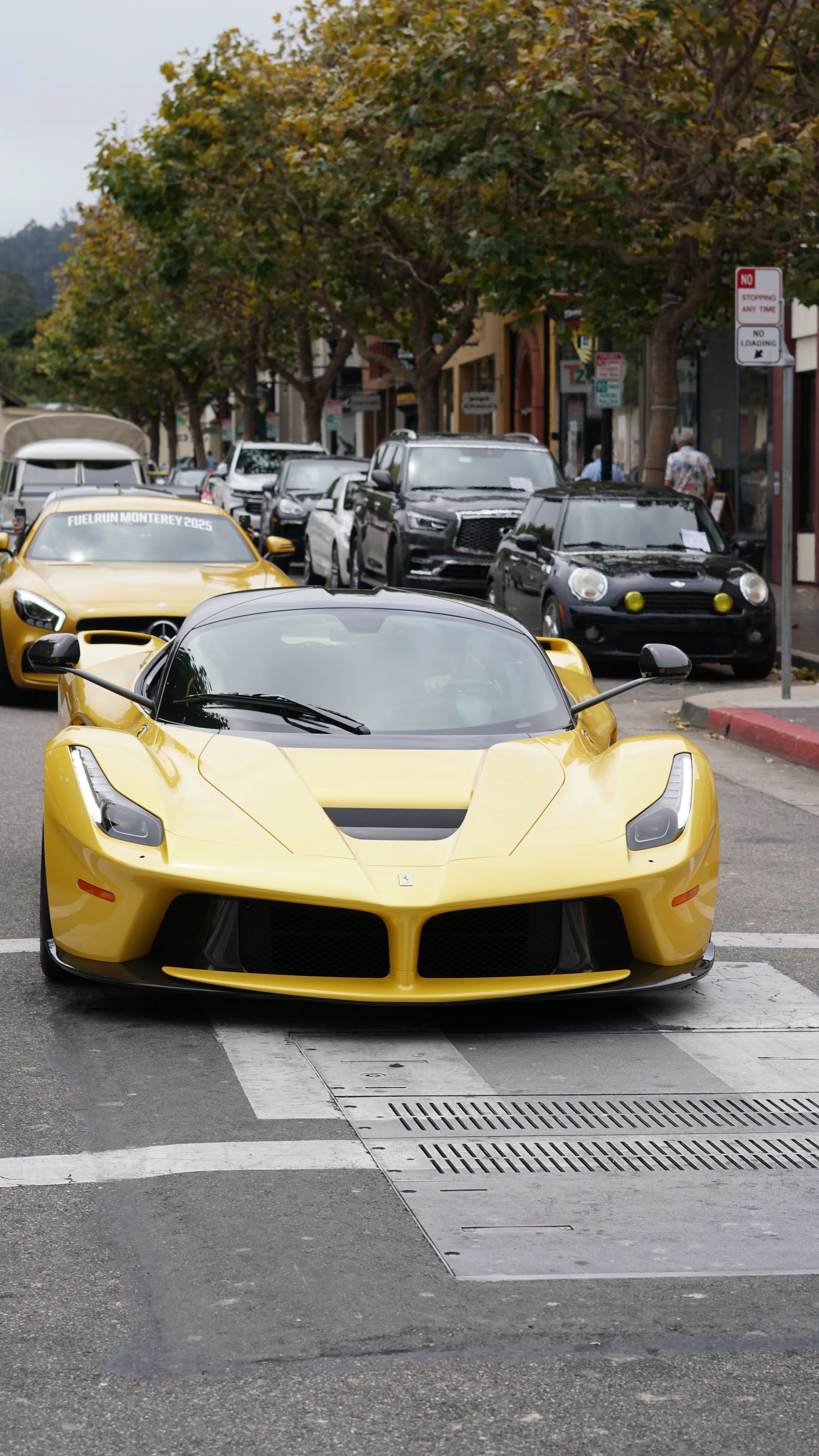 A yellow sports car parked in the street with other cars and trees in the background.