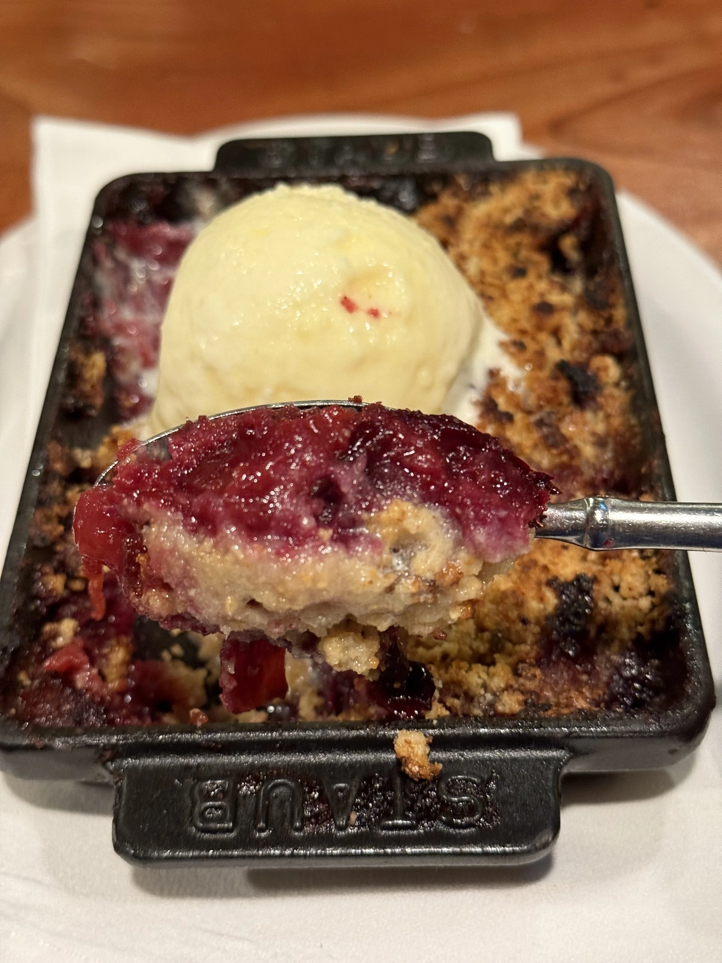 A serving of cherry cobbler with a scoop of vanilla ice cream on top, served in a small black skillet on a white plate.