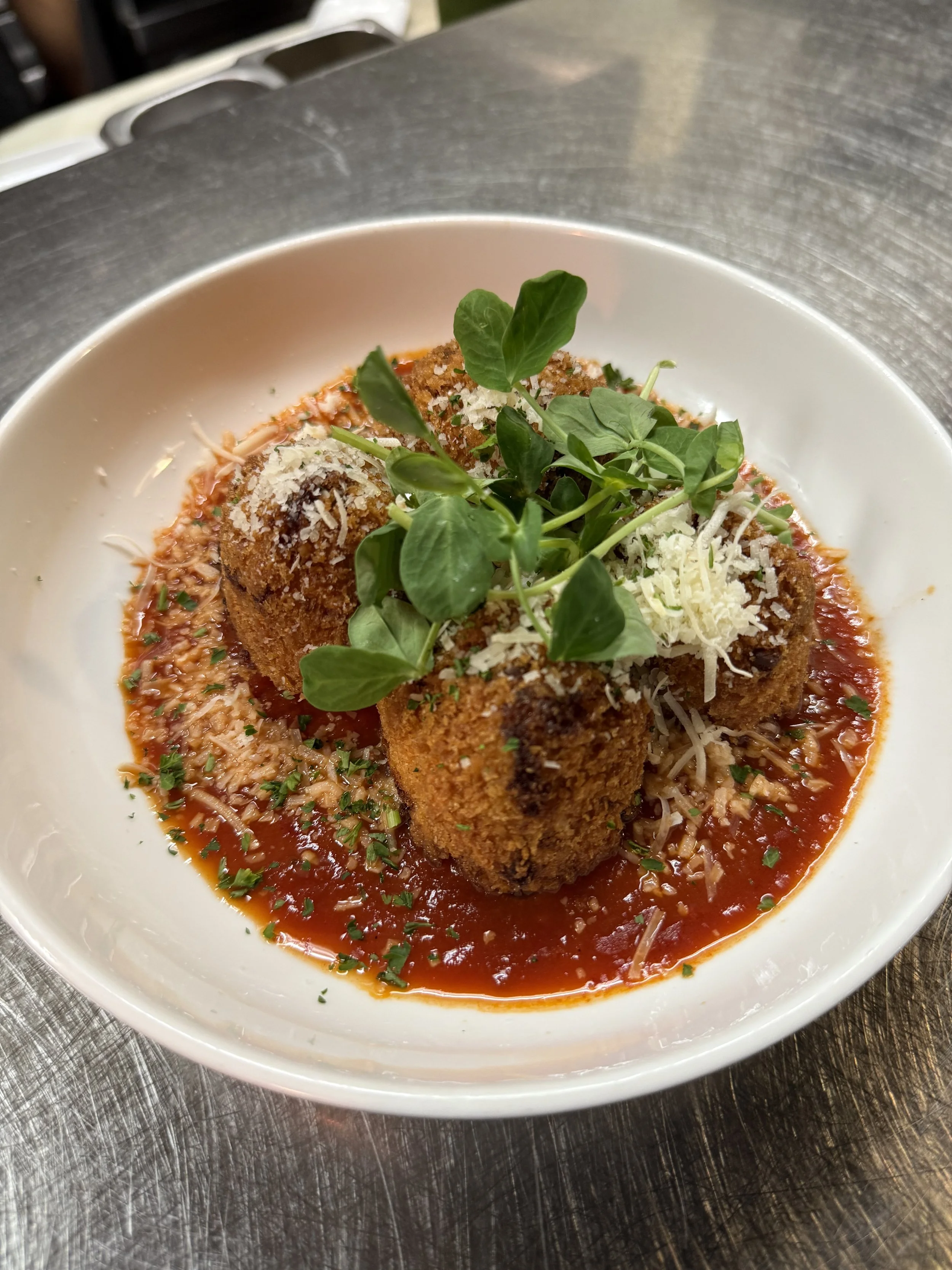 Fried mozzarella sticks with marinara sauce, topped with shredded cheese and microgreens
