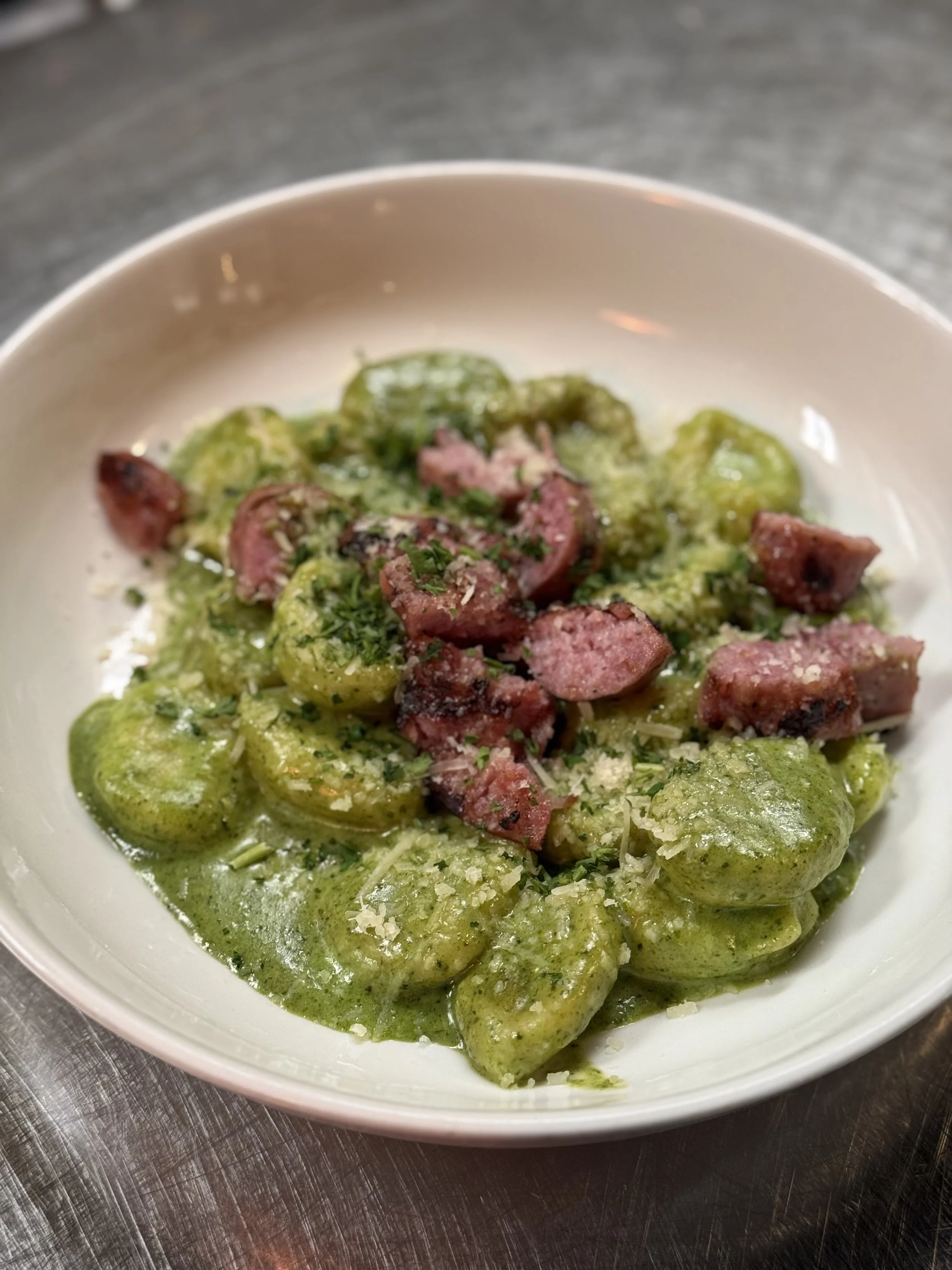 Plate of green spinach gnocchi topped with chopped meat and grated cheese.