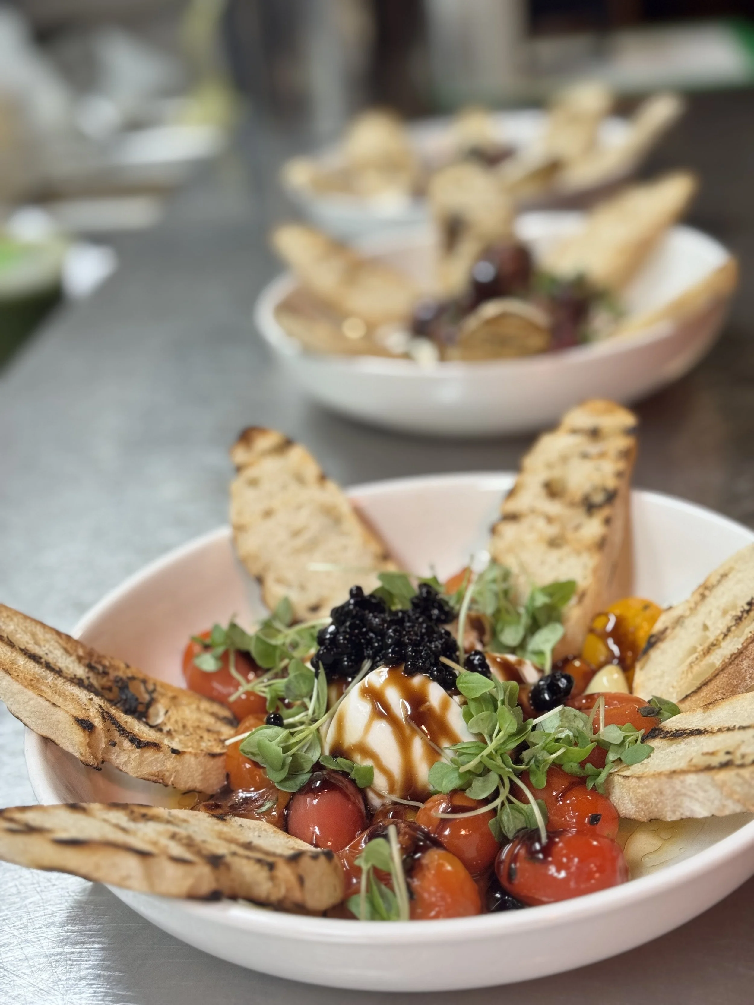 Caprese salad with cherry tomatoes, basil, mozzarella, balsamic glaze, green microgreens, and toasted bread slices in a white bowl.