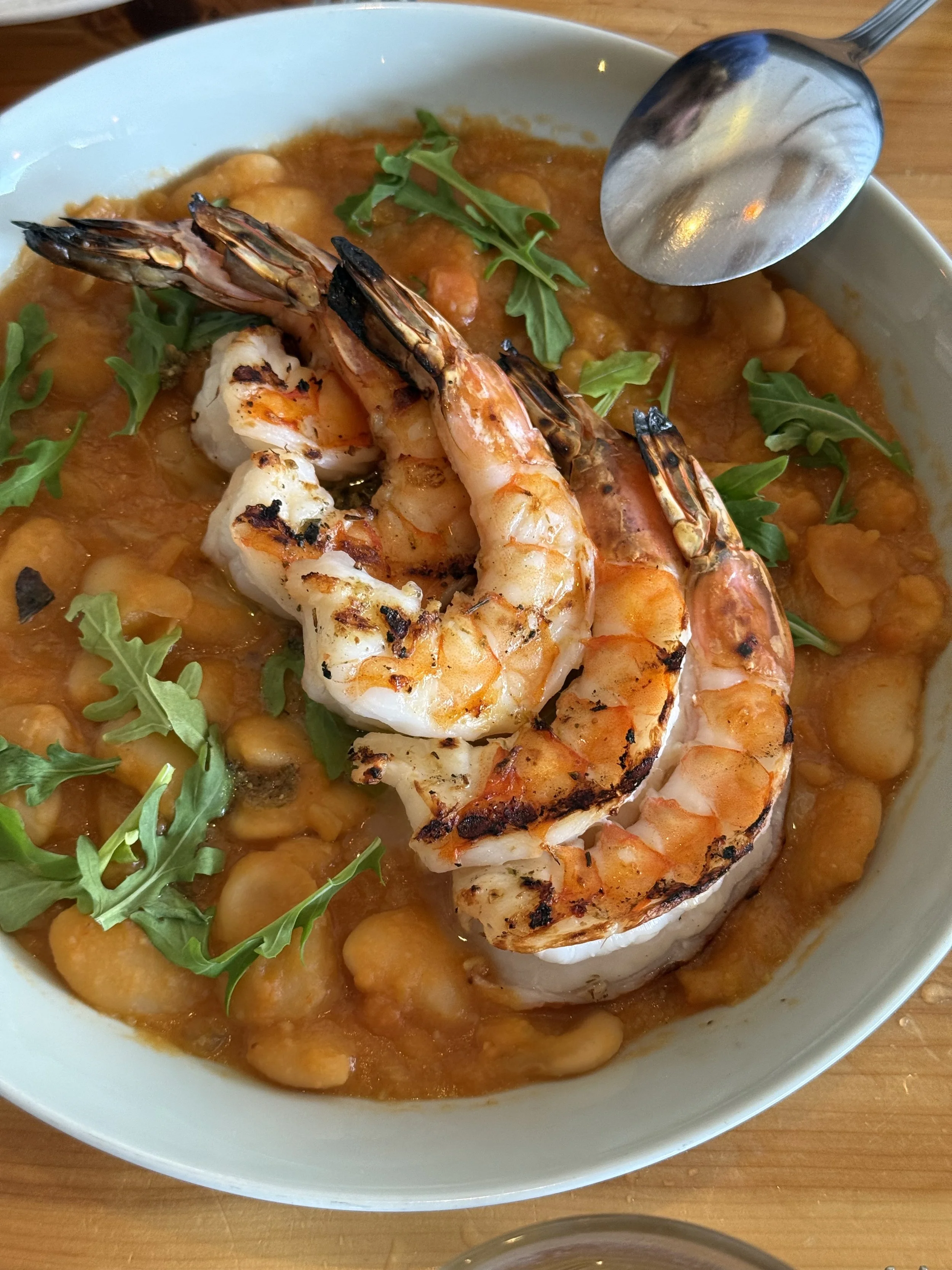 Bowl of chickpea stew with grilled shrimp and arugula garnishing.