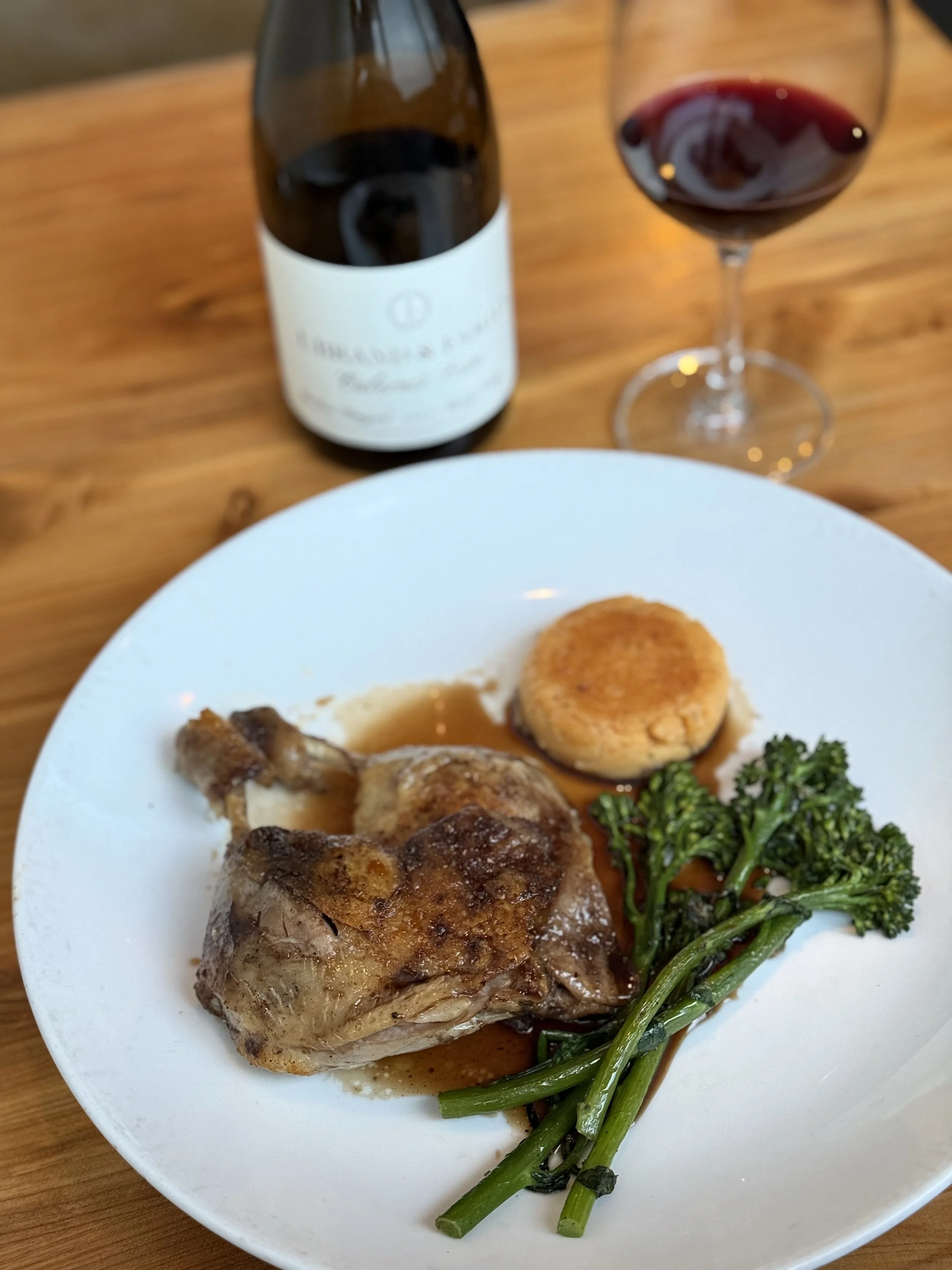 A white plate with a cooked chicken thigh, a small round baked dish, a bunch of cooked broccoli, and a brown gravy.