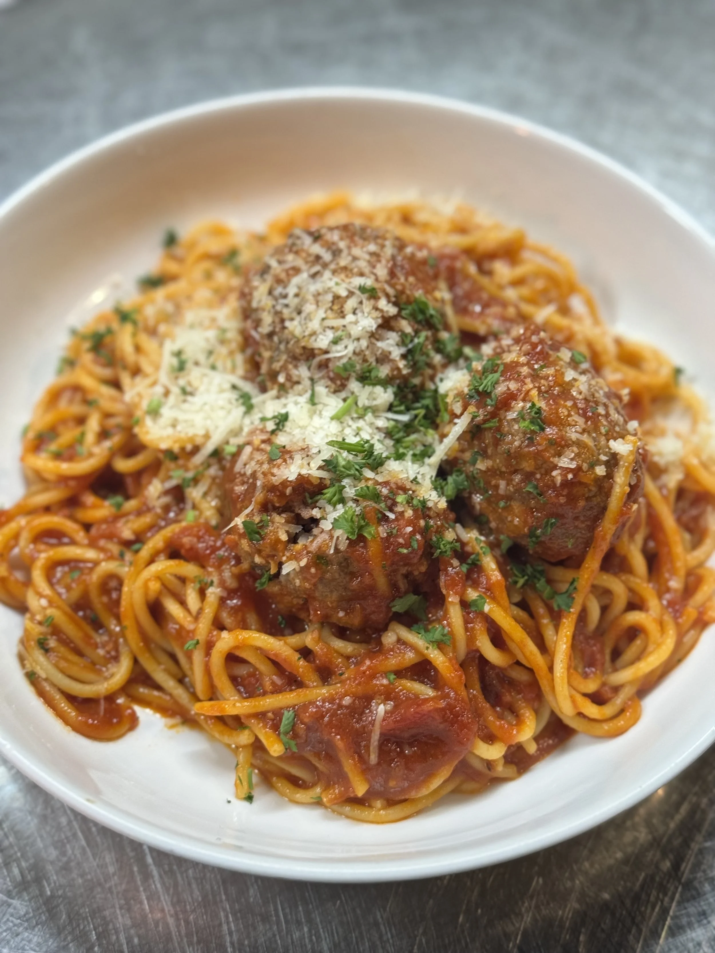 Bowl of spaghetti with meatballs topped with grated cheese and chopped parsley.